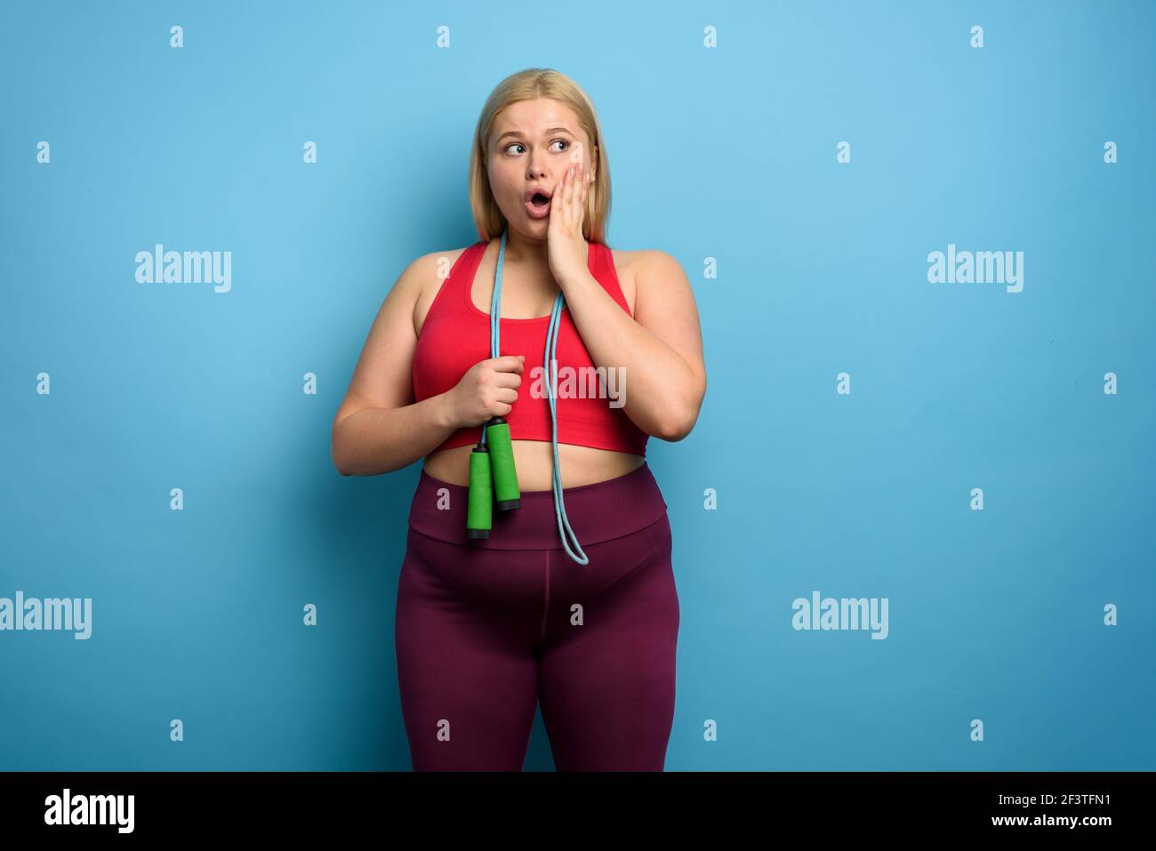 Fat Mädchen tut Fitness-Studio, aber ist besorgt für etwas. Cyan Hintergrund Stockfoto