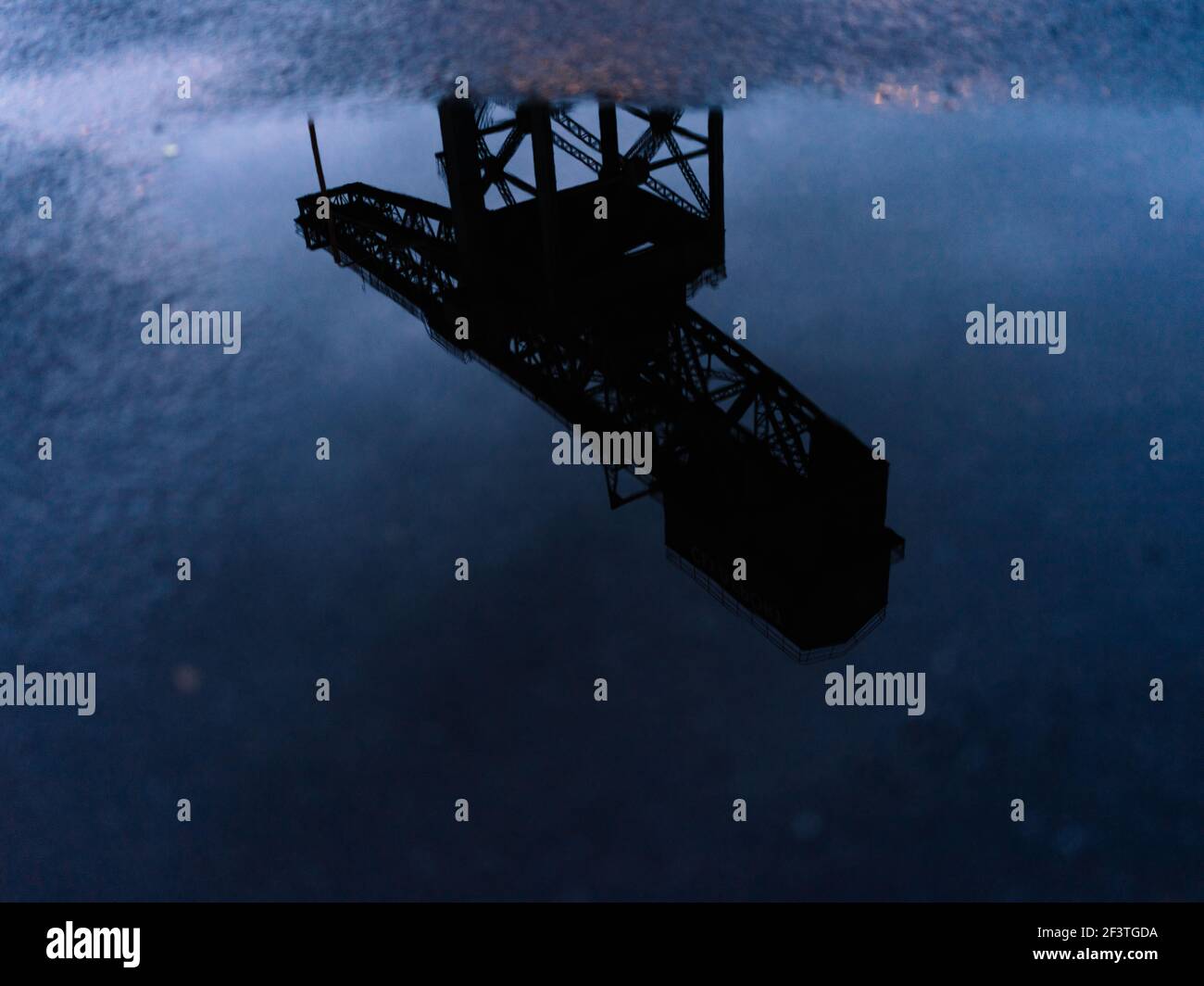 Alternative Ansicht des ehemaligen Clydeside Schiffbaus Finnieston Crane, bekannt als Titan, reflektiert in Pfützen in der Dämmerung, Glasgow, Schottland. Stockfoto