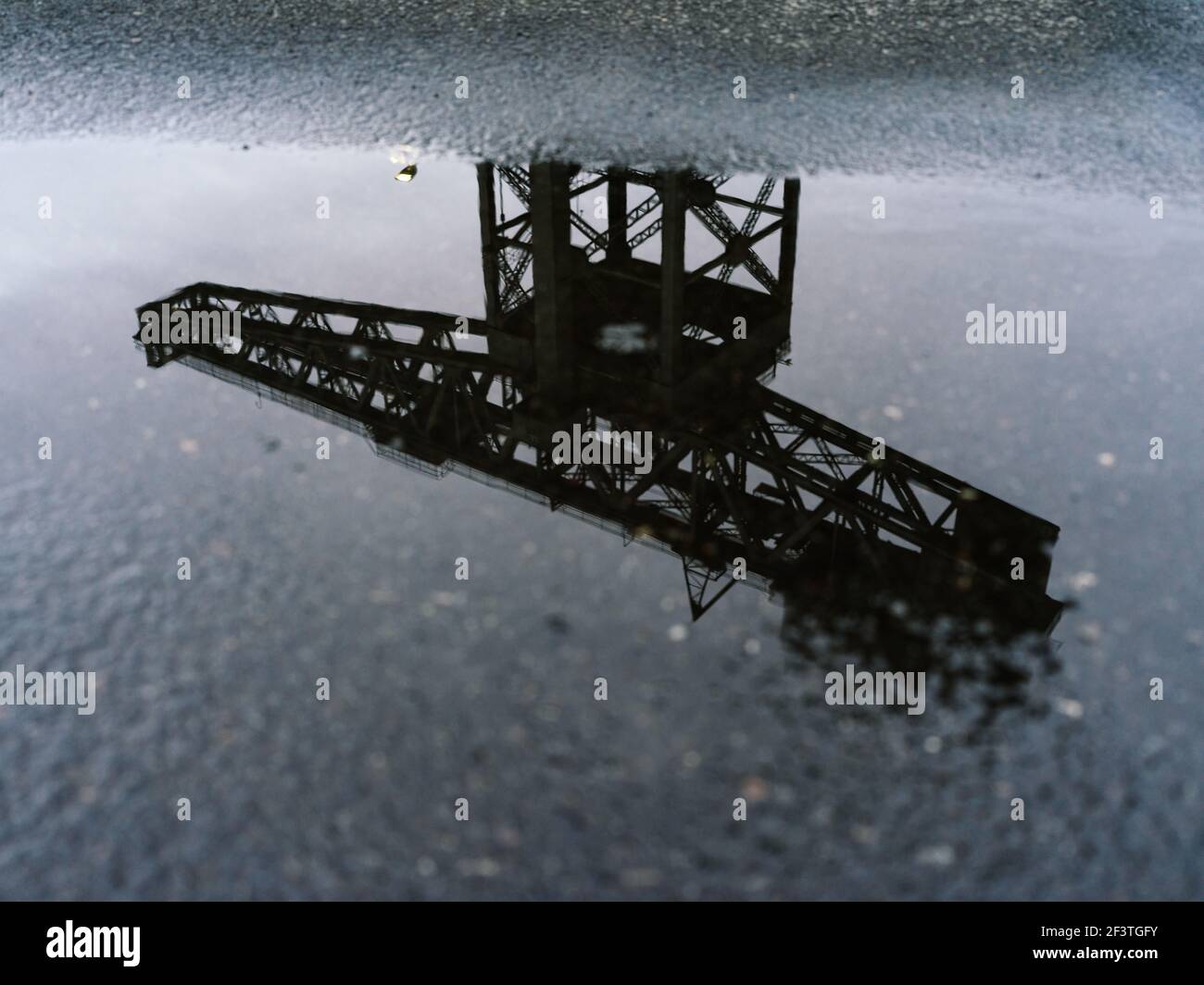 Alternative Ansicht des ehemaligen Clydeside Schiffbaus Finnieston Crane, bekannt als Titan, reflektiert in Pfützen in der Dämmerung, Glasgow, Schottland. Stockfoto