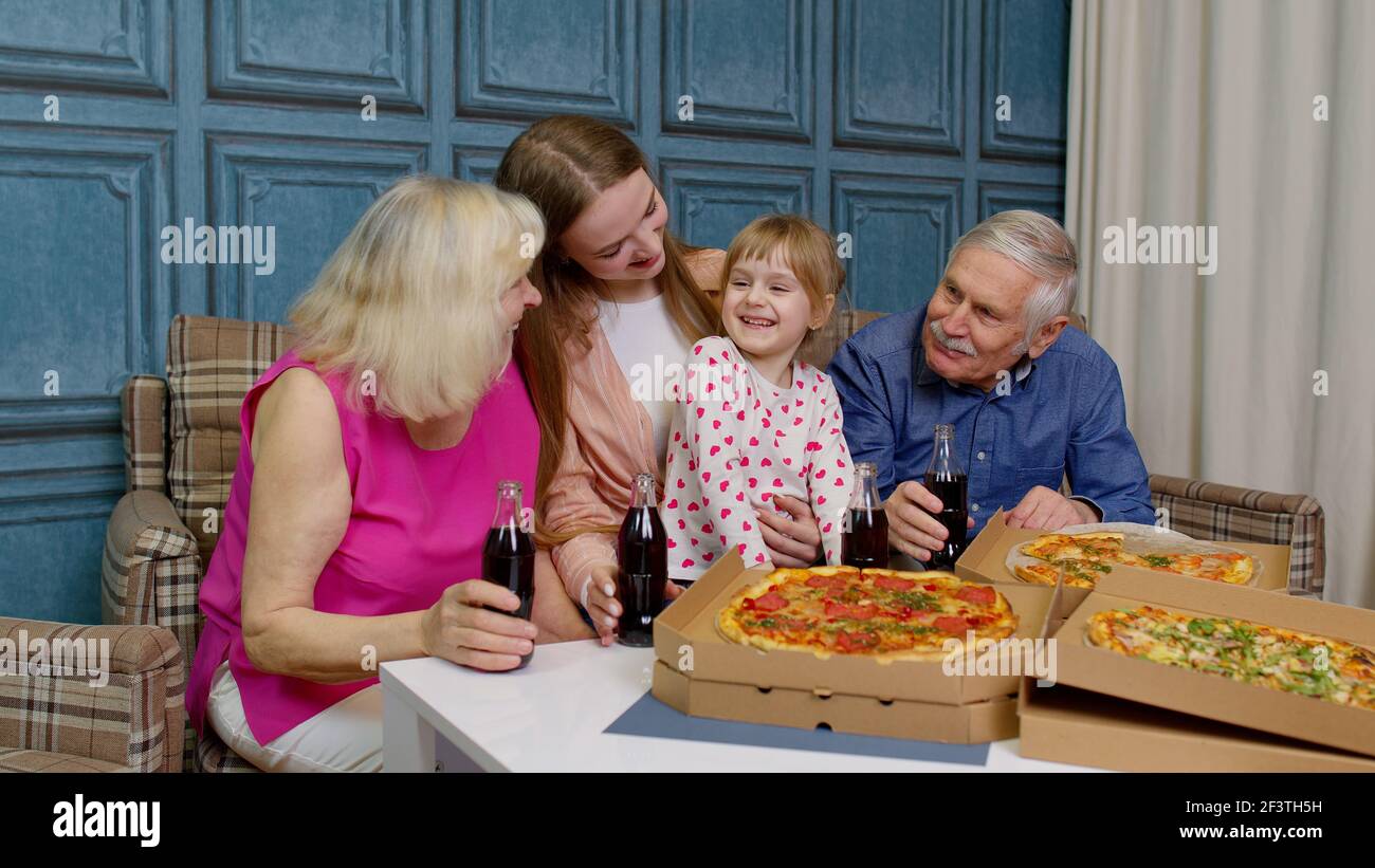 Glückliche Familie mit mehreren Generationen, die zu Hause eine Mittagsparty macht, Pizza isst und gemeinsam Toast macht Stockfoto