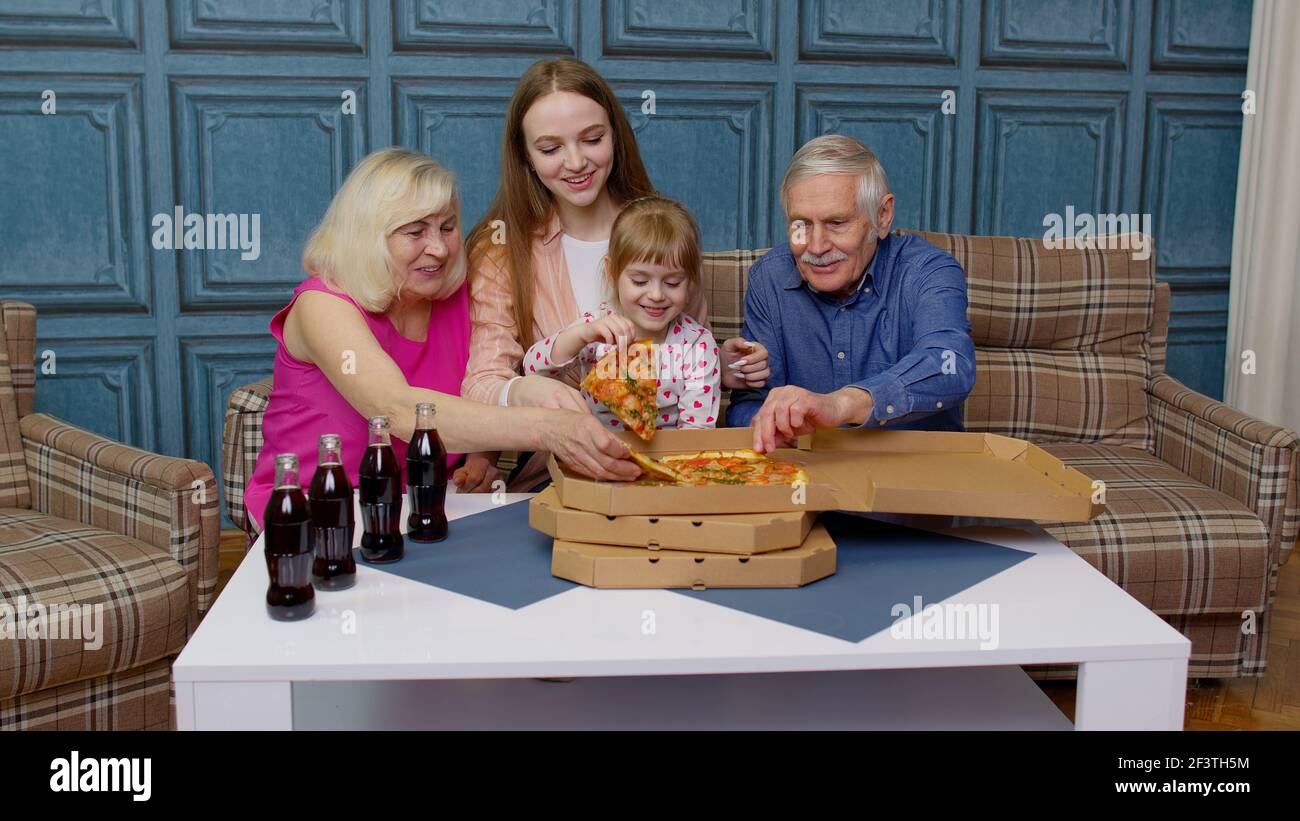 Glückliche Familie mit mehreren Generationen, die zu Hause eine Mittagsparty macht, Pizza isst und gemeinsam Toast macht Stockfoto
