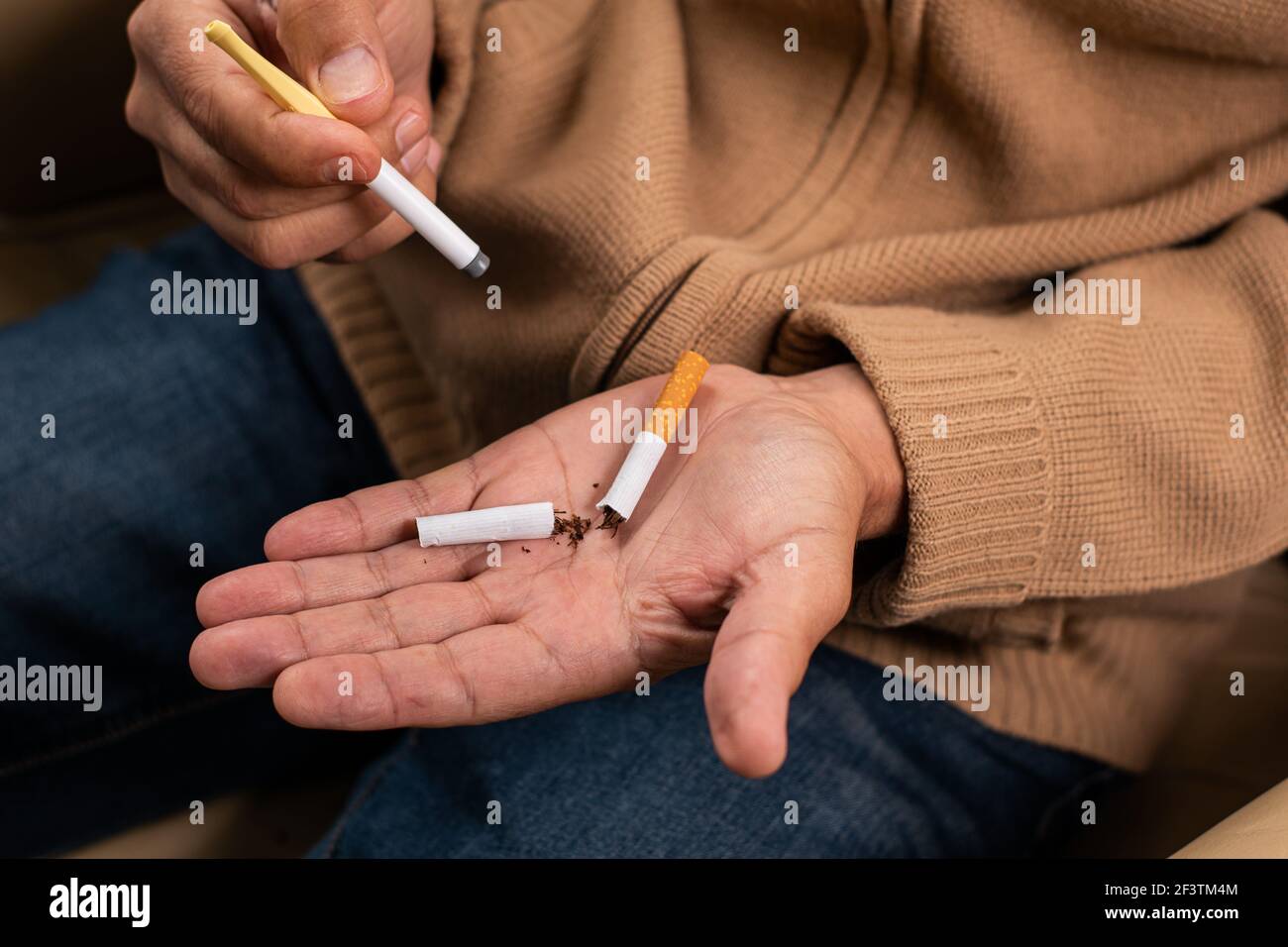 Detailaufnahme der faltigen Hände eines Mannes, der eine Plastikzigarette hält, um mit dem Rauchen aufzuhören, und in der anderen eine zerbrochene Zigarette, die Tabak ablehnt. Stockfoto