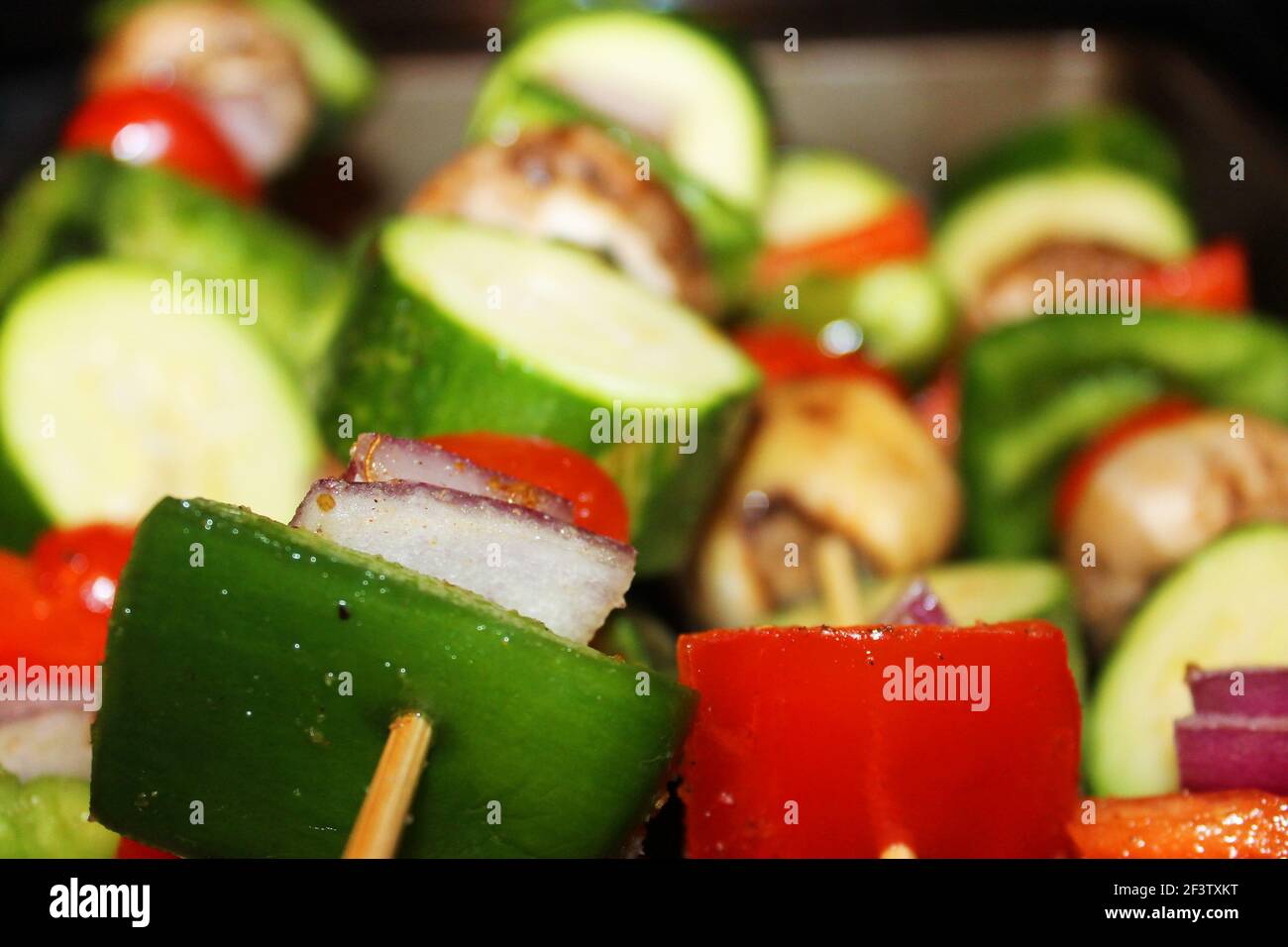 Nahaufnahme von rohen Gemüsespießen, mit grünem Pfeffer, rotem Pfeffer, Zucchini, Pilzen, Rote Zwiebel, Kirschtomate und Gewürze. Stockfoto