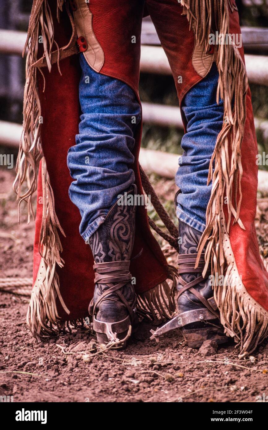 Die gefransten Lederknaben und Cowboystiefel mit den Spornen eines Cowboys beim Stierreiten in einem Kleinstadt-Rodeo in New Mexico. Stockfoto