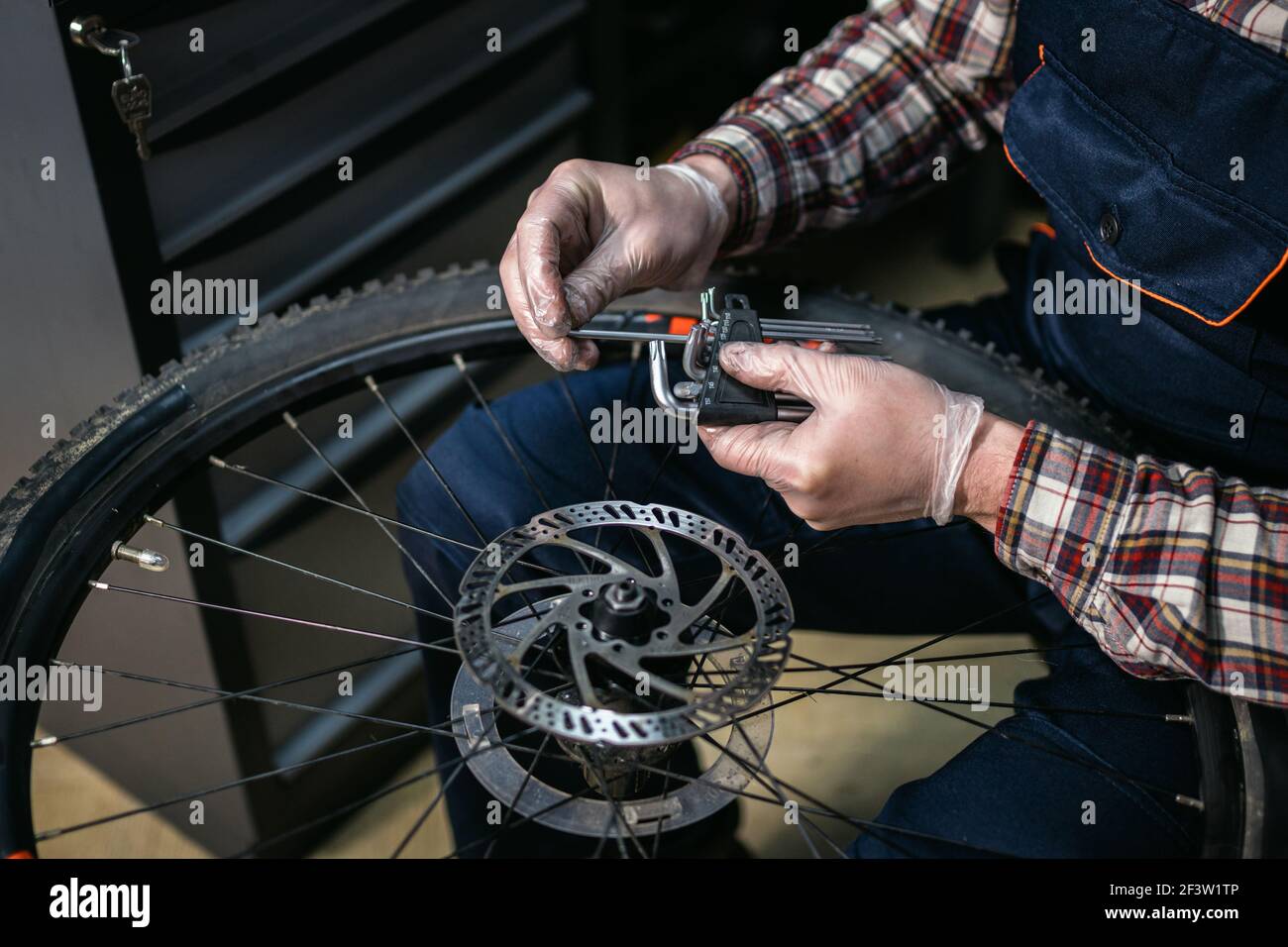 Technisches Know-how, die Pflege Fahrrad-Shop. Handsome junge Mechaniker Befestigung Rad in der Werkstatt. Gut aussehende Werkstatt in Arbeitskleidung serviert Berg Stockfoto