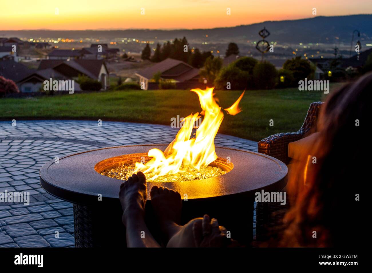 Eine Frau entspannt sich bei Sonnenuntergang bei einem knisternden Feuerresten auf einer Feriterasse mit Blick auf das Spokane Valley im US-Bundesstaat Washington Stockfoto