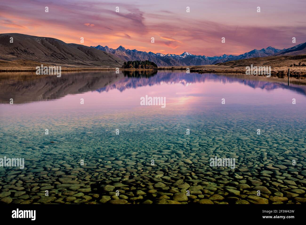 Transparant kristallklares Wasser zeigt die Felsen auf dem Boden Des Sees mit Bergreflexionen bei Sonnenuntergang Stockfoto