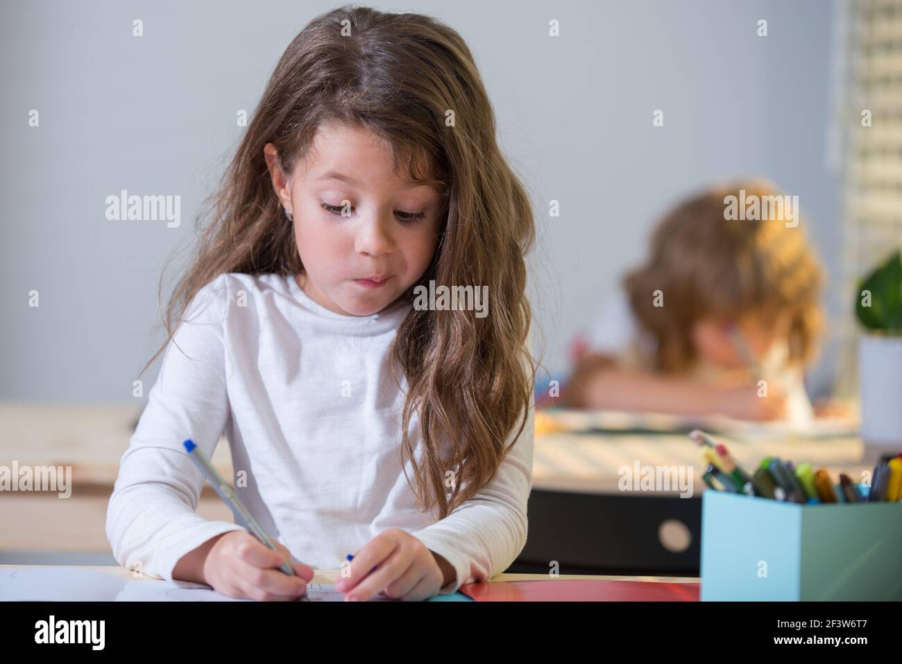 Lustige Schüler im Klassenzimmer in der Schule. Kleines Mädchen, das im Unterricht am Schreibtisch sitzt. Portrait der jungen Schülerin studieren und schreiben auf Notebook. Konzentriert Stockfoto