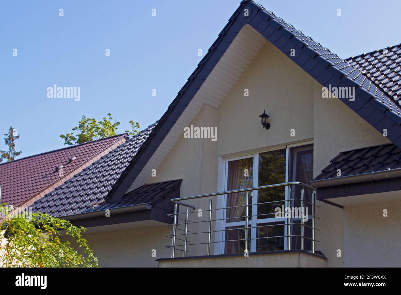 Stilvoller Balkon unter einem dreieckigen blauen Dach aus blauem Metall Fliesen mit Chromgeländer und eine Laterne Wandleuchte über die Tür im zweiten Stock von zwei sto Stockfoto