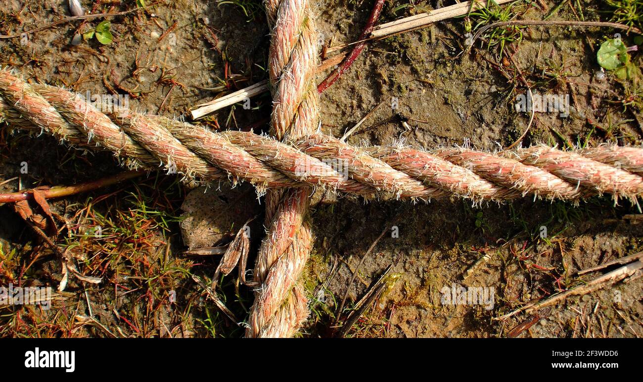 Ein Kreuz aus Seilen. Detail eines alten verwitterten Seils auf dem Boden. Die Farbe des Seils war einst rot. Stockfoto