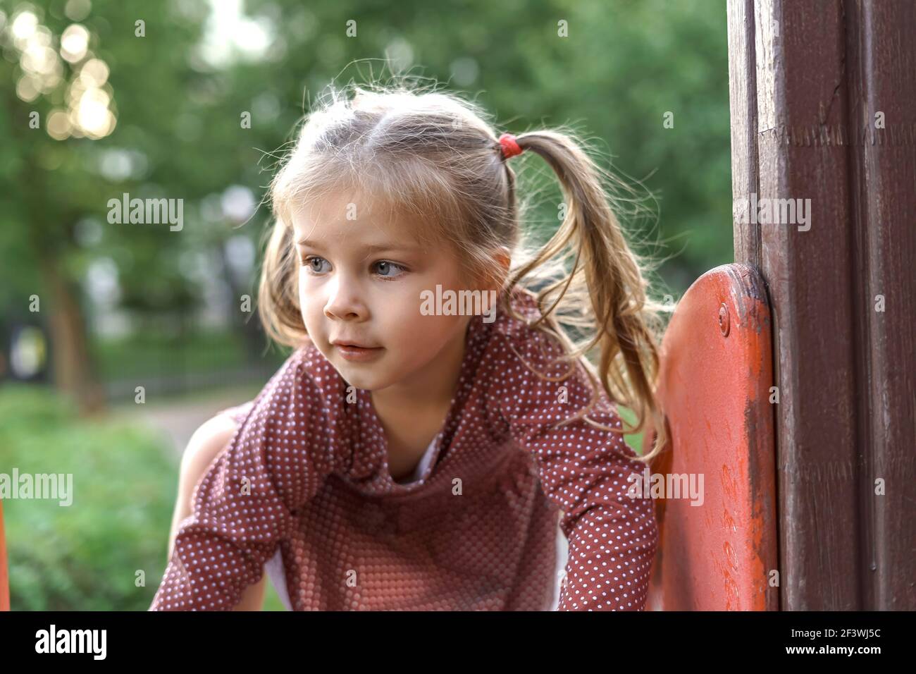 Kleines Mädchen in roten Kleid spielt auf dem Spielplatz an einem Sommertag. Gesunde Sommeraktivitäten für Kinder. Stockfoto