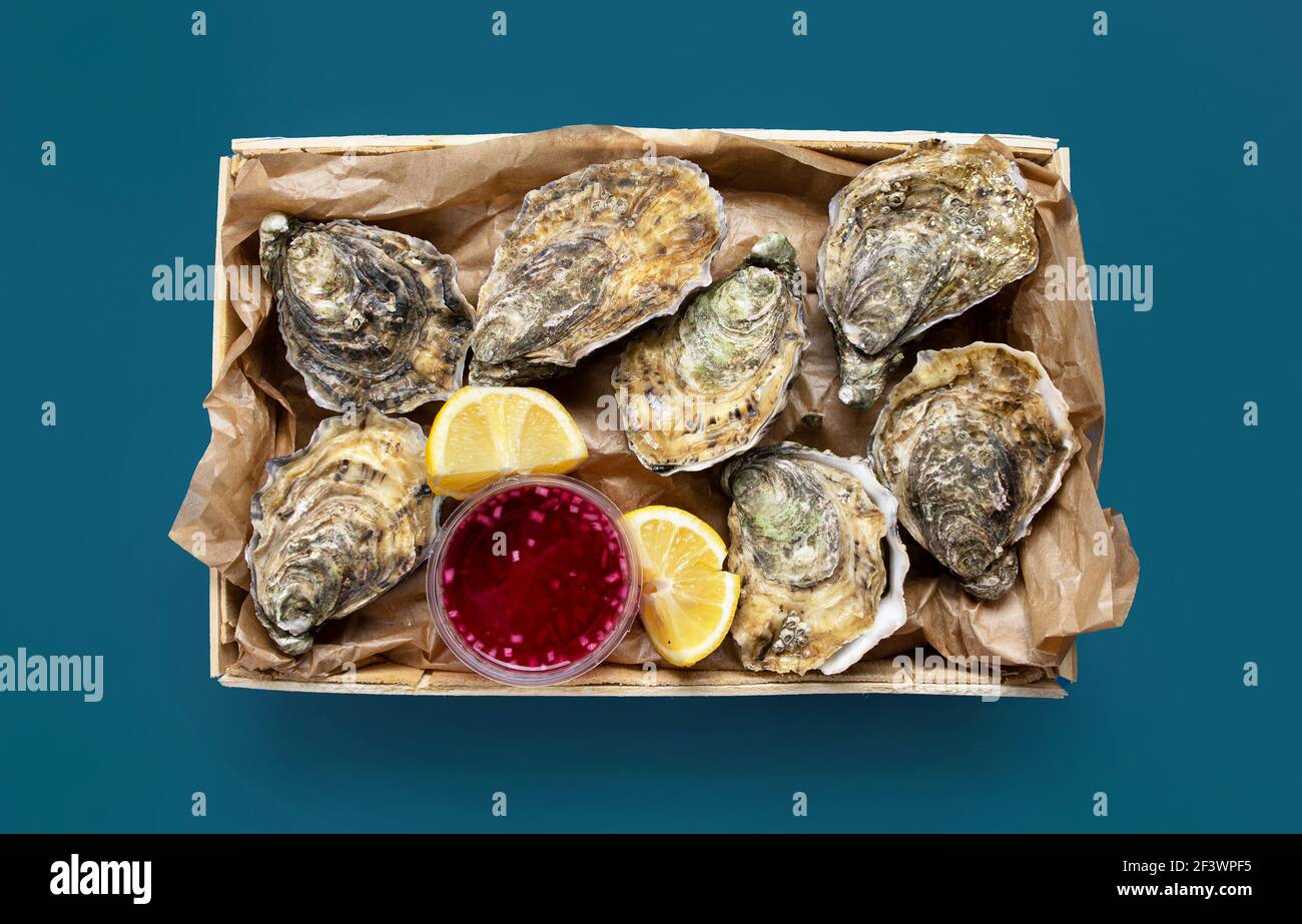 Schachtel mit geöffneten frischen Austern, Zitrone und Essig Zwiebelsouce auf blauem Hintergrund, Draufsicht Stockfoto