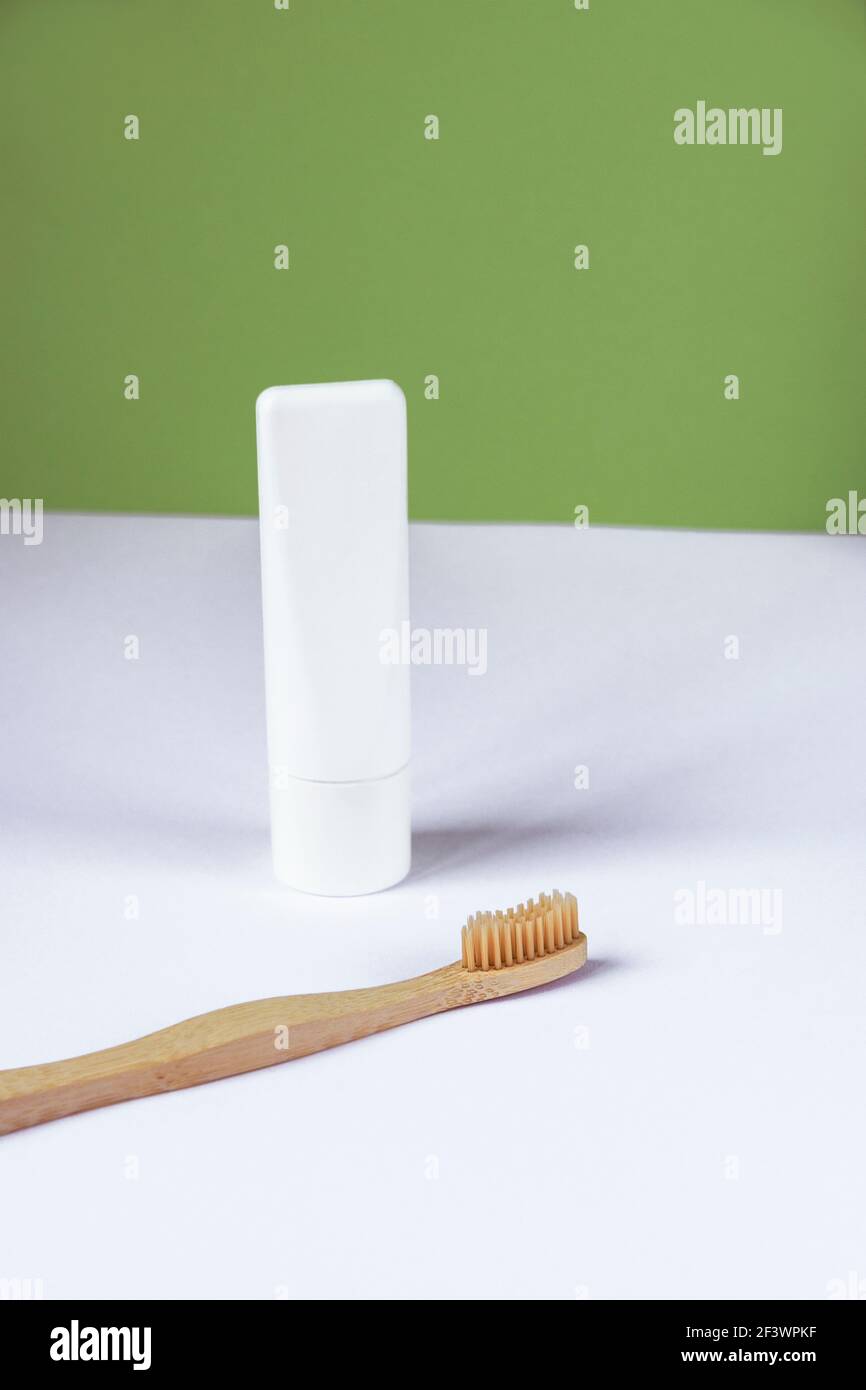 Weiße Tube Zahnpasta und Zahnbürste auf weißem Tisch vor grünem Wandhintergrund. Persönliche Hygiene und Self-Care-Konzept. Vorderansicht. Stockfoto