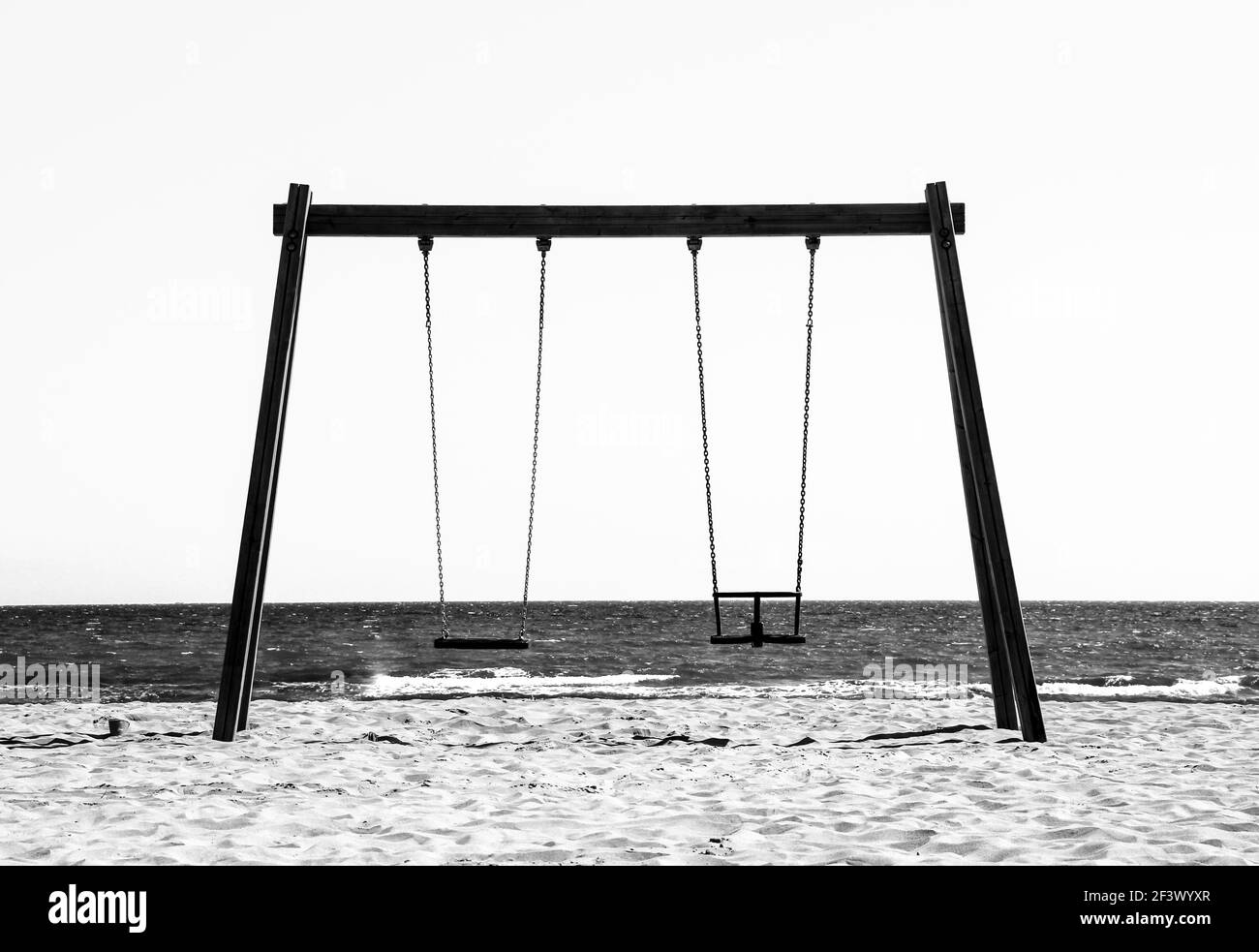 Leere Holzschaukel mit Blick auf das Meer am Morgen in Alicante, Spanien. Monochromes Bild. Stockfoto