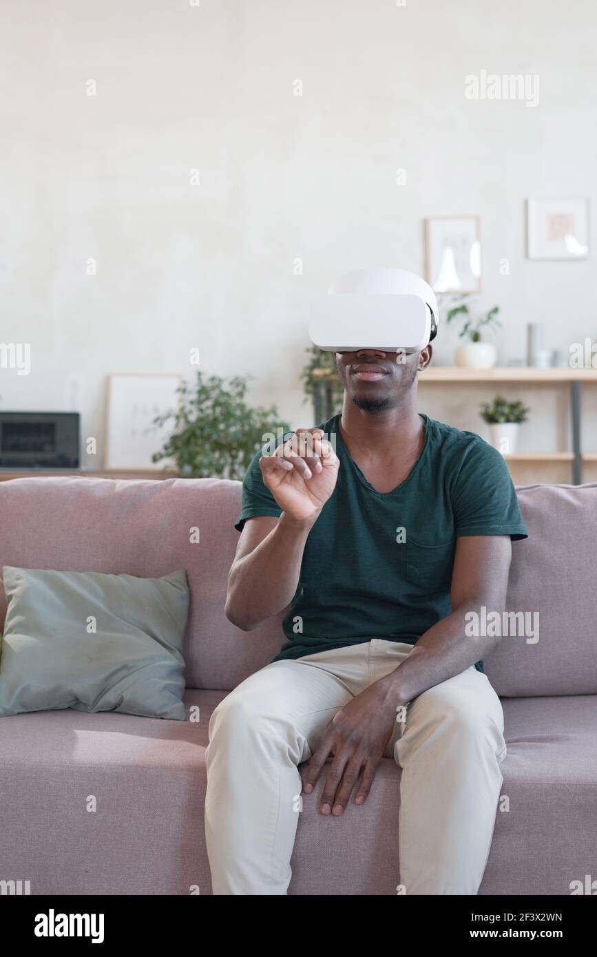 Afrikanischer Mann sitzt auf dem Sofa und mit VR-Brille Zu Hause Stockfoto