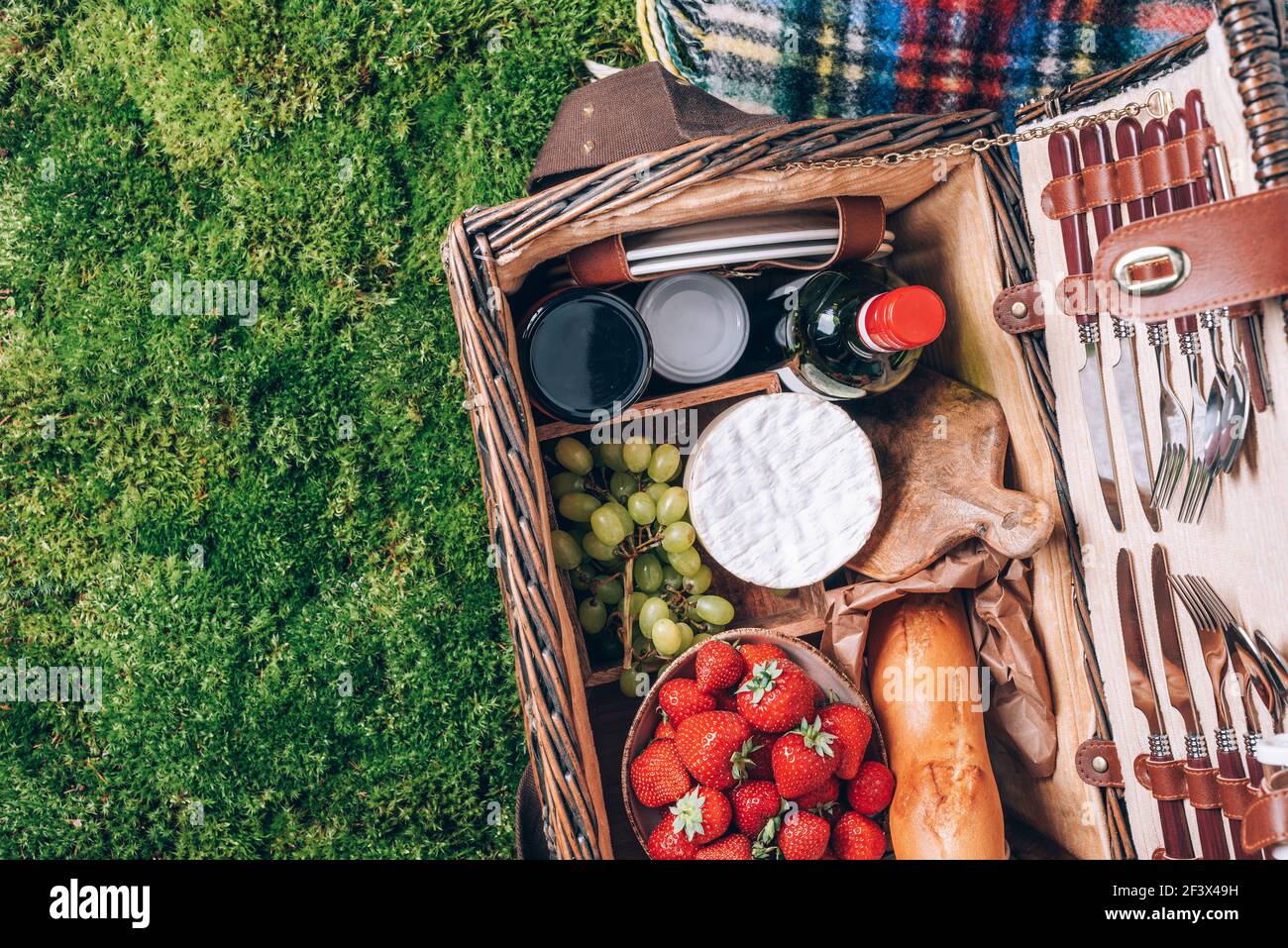 Toller Picknickkorb mit Käse, Erdbeeren, Trauben, Baguette, Wein zum Picknick auf karierten grünen Hintergrund. Draufsicht. Speicherplatz kopieren. Sommerfamilie Stockfoto
