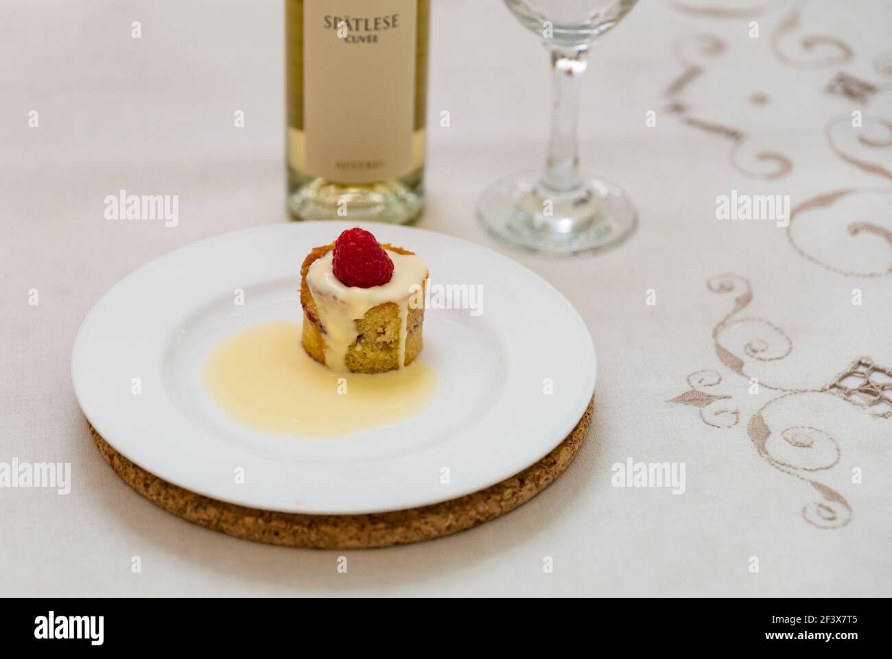 Mandelkuchen mit Pudding und Himbeere auf Weiß serviert Teller mit Flasche österreichischen Kracher Cuvee Auslese weißen Dessert Wein Stockfoto