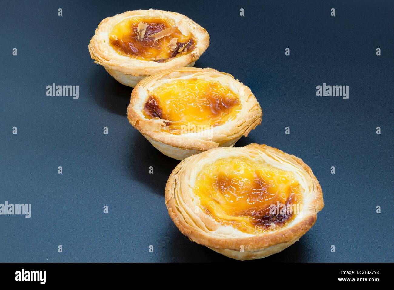 Drei kleine Pudding-Tarts auf dunkelgrauem Hintergrund. Stockfoto