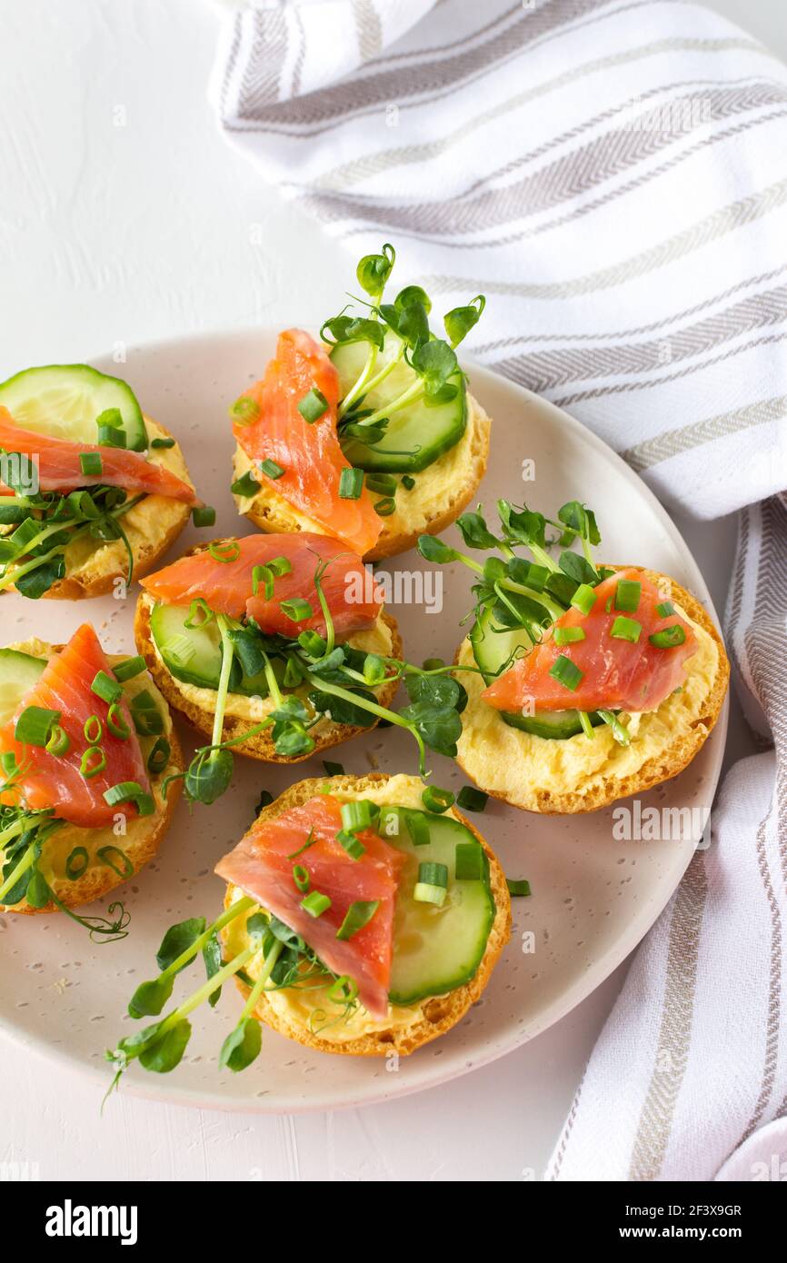 Leckere herzhafte Vorspeise, Lachsbraten auf einem weißen Teller, rundes gebratenes Brötchen mit rotem Fisch, Gurke, Sauce Hollandaise und Erbsensprossen Stockfoto