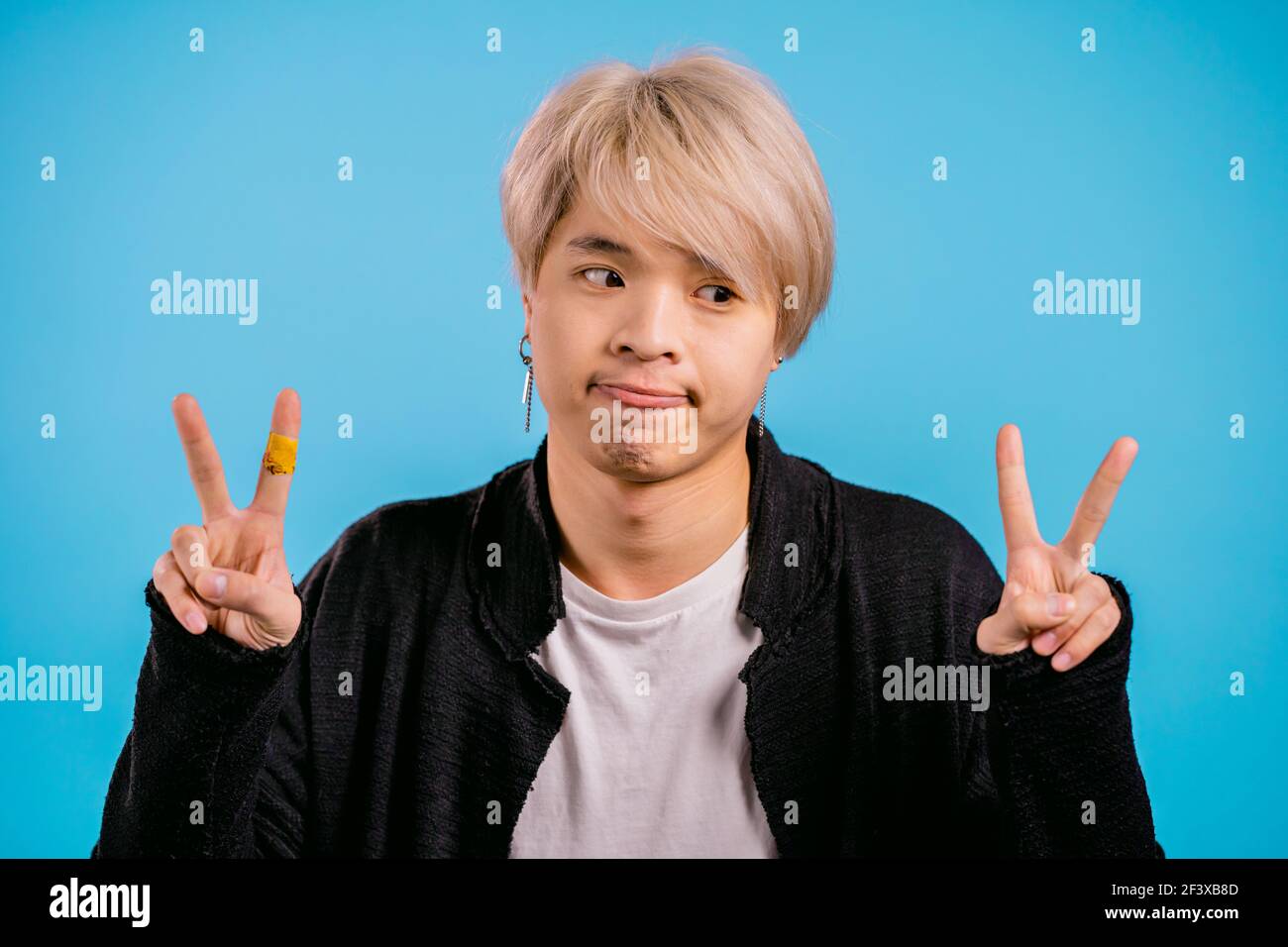 Asiatischer Mann zeigt mit Händen und zwei Fingern Luft Zitate Geste, biegen Finger isoliert auf blauem Hintergrund. Nicht lustig, Ironie und sarkastisch Konzept. Stockfoto