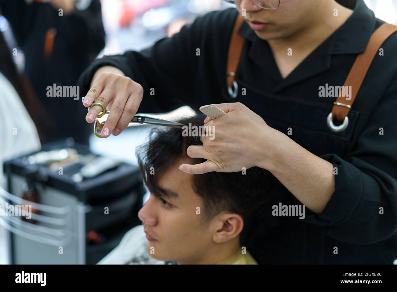 Barber trimmt die Haare eines jungen Mannes mit einer Schere In seinem Friseurladen Stockfoto