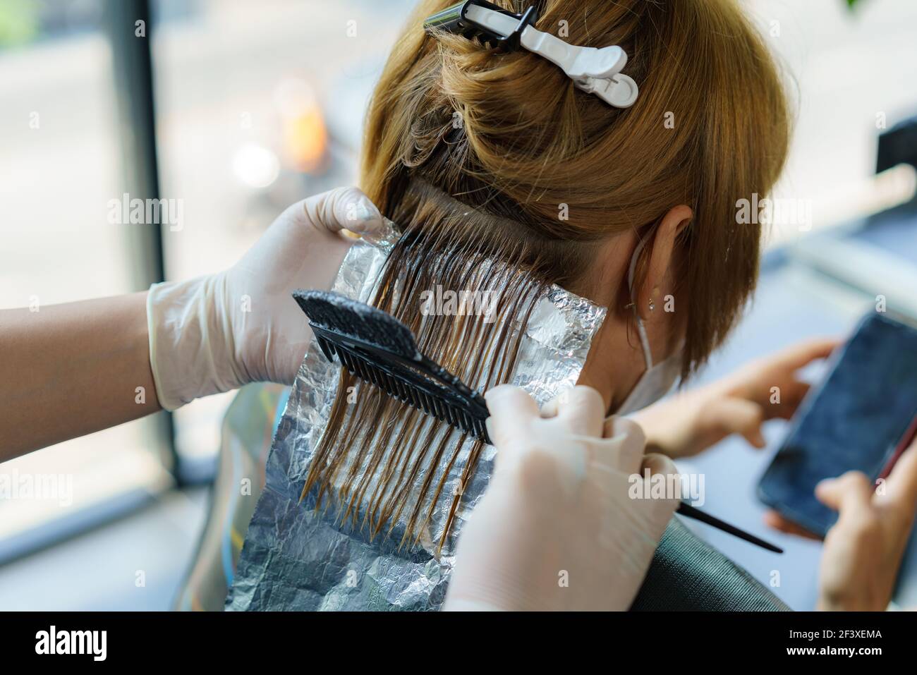 Attraktive Brünette gründlich färben Haare der weiblichen Klienten, während sie im Stuhl sitzt im Beauty Salon Friseur Stockfoto