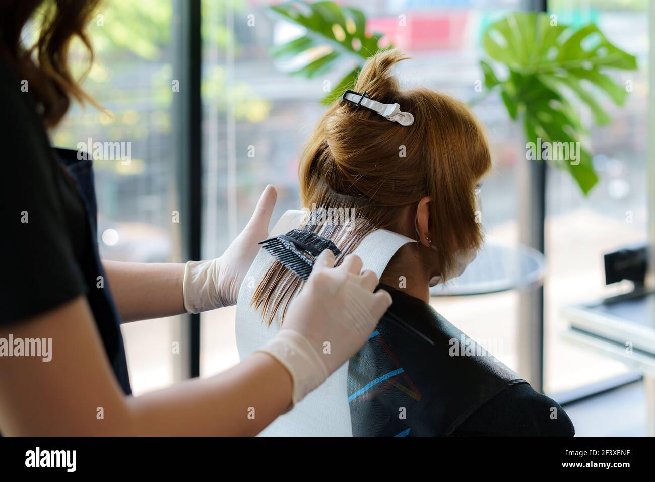 Attraktive Brünette gründlich färben Haare der weiblichen Klienten, während sie im Stuhl sitzt im Beauty Salon Friseur Stockfoto