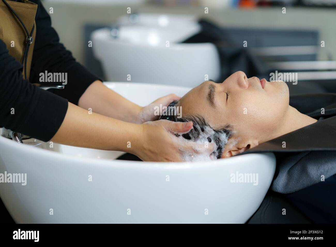 Friseur Anwendung Shampoo und massieren Haar eines Kunden. Mann, der seine Haare in einem Friseursalon gewaschen. Stockfoto