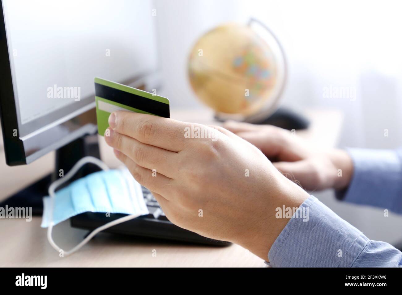 Mann mit Kreditkarten-Typen auf PC-Tastatur. Konzept des Online-Einkaufs und Zahlung, Kauf einer Reise-Tour während Coronavirus-Pandemie Stockfoto