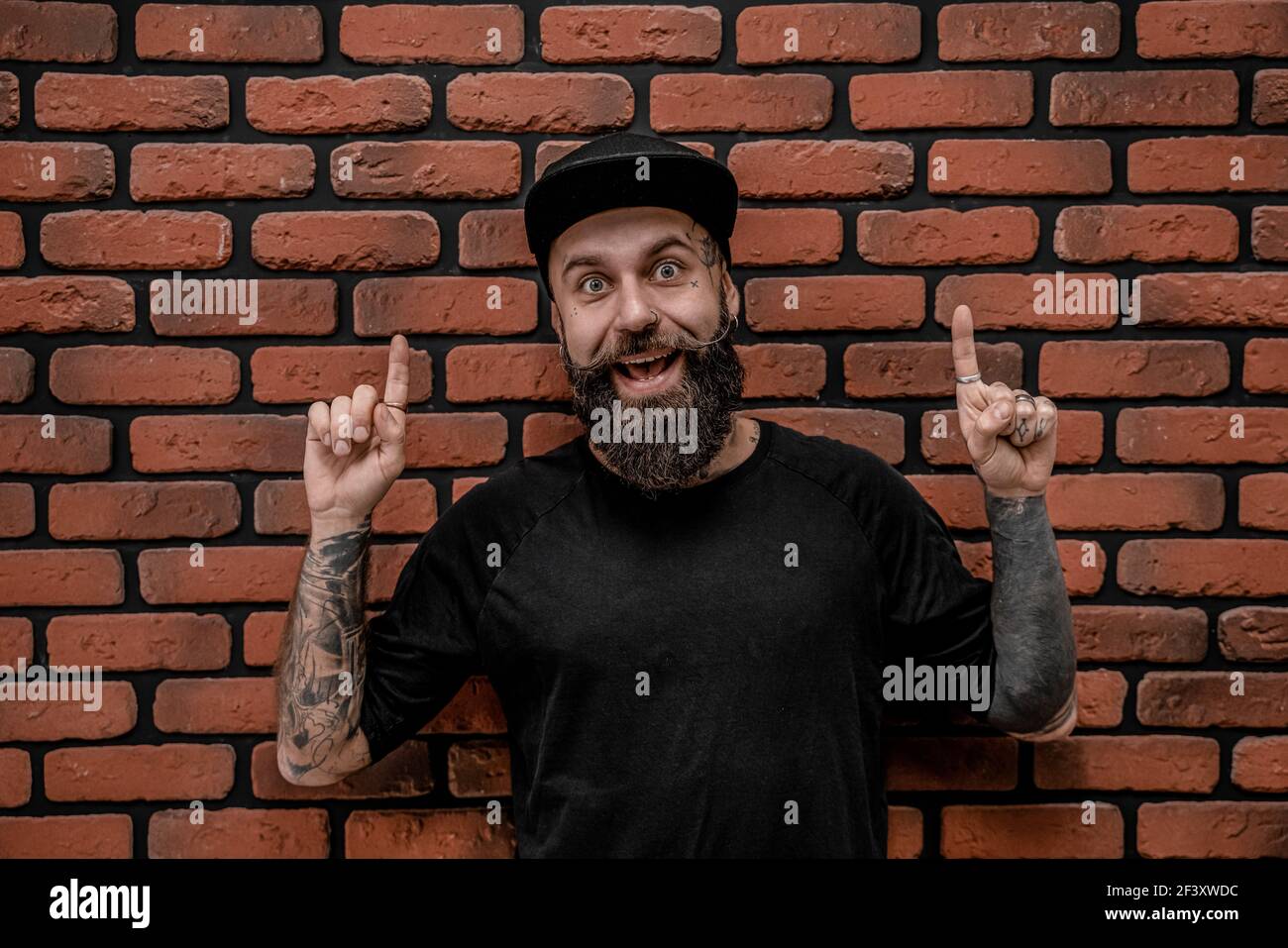 Gutaussehende altmodische Hipster in T-Shirt und Mütze, Pose lustig und lächeln. Auf einem Backstein Hintergrund. Stockfoto