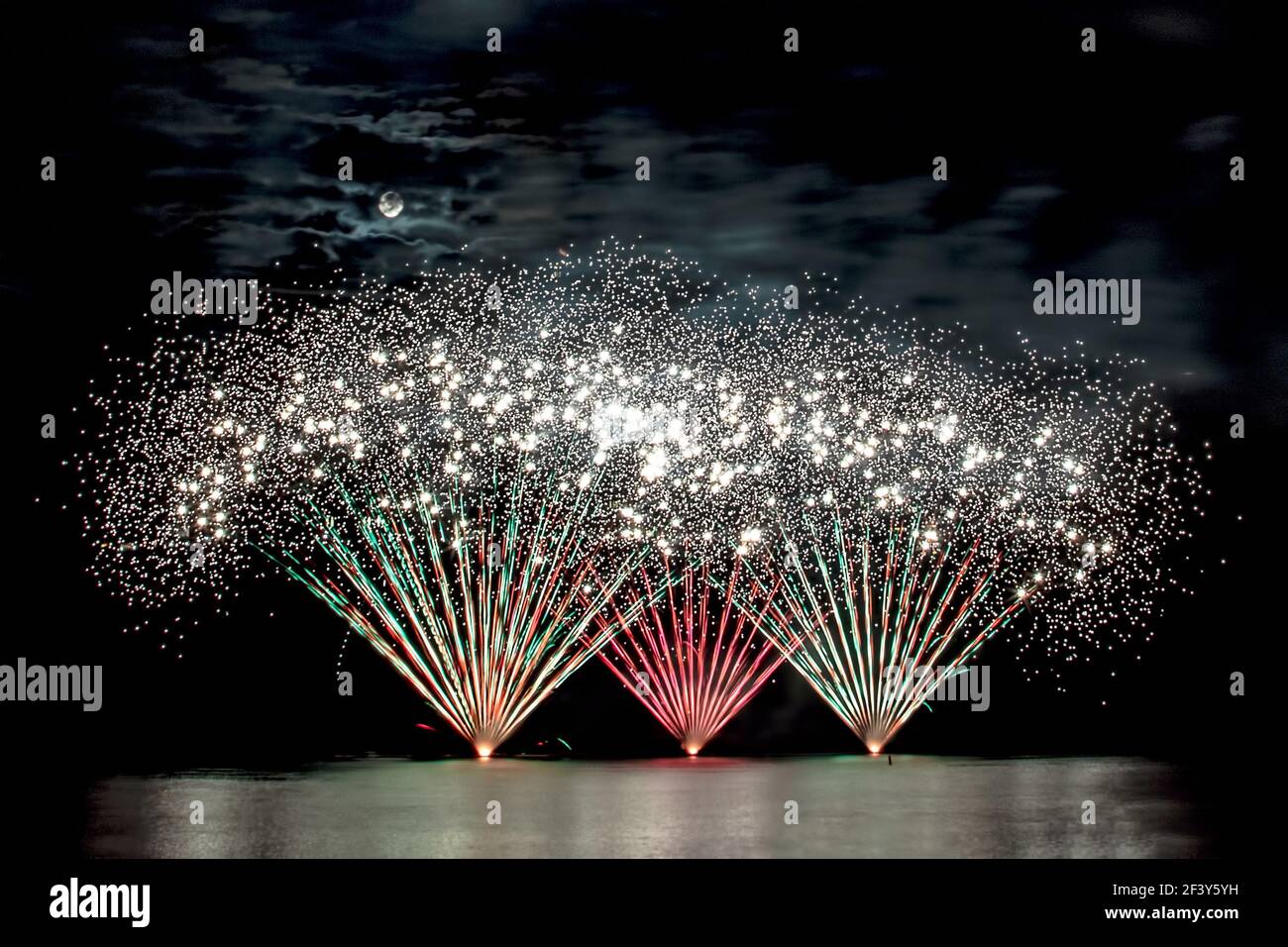 Schillerndes Feuerwerk bei einem Sommerfeuerwerk Wettbewerb - die Vollmond scheint durch die Wolken Stockfoto