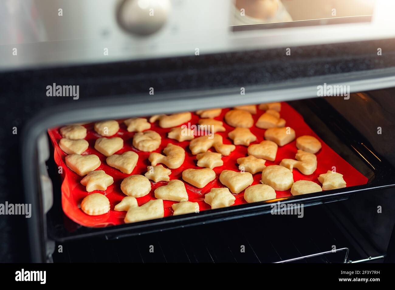 Süß lecker leckeren Quark Ingwer Cookies Backen im heißen Ofen Herd auf Tablett und rot hellen Silikon Backmatte in der heimischen Küche. Hausgemachte heiße Kekse Stockfoto