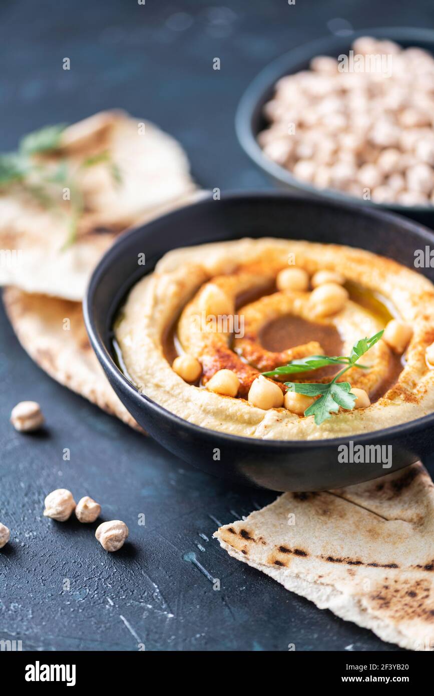 Hummus, Kichererbsen-Dip, Olivenöl, rohe Bohnen, geräucherter Paprika, Pita auf dunklem authentischem Hintergrund. Nahöstliche, jüdische Küche oder arabische Gerichte. Oben Stockfoto