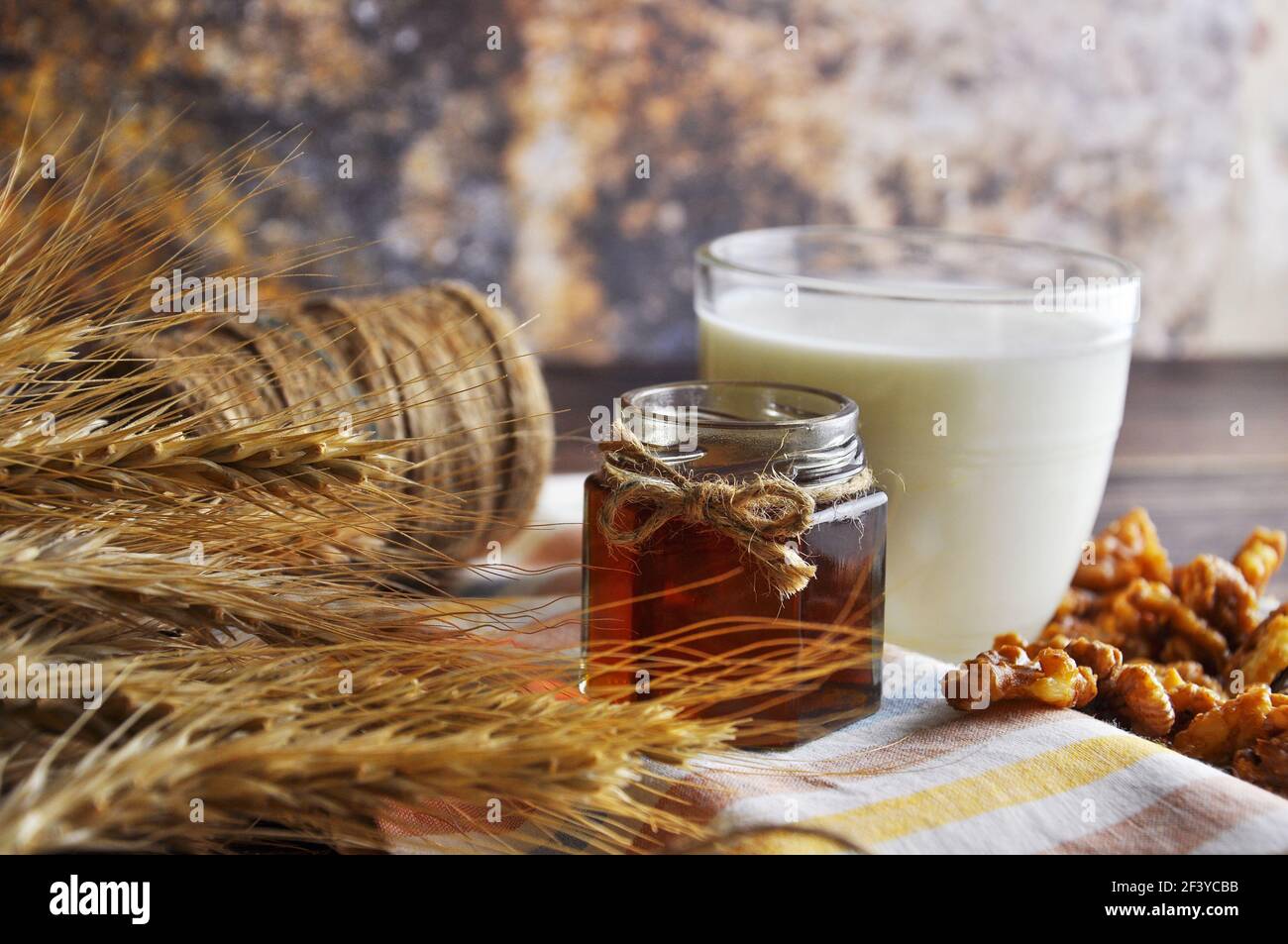 Offenes Glas mit flüssigem Honig, Milch, Nüssen, Weizen auf dem Vintage Handtuch. Hintergrundlayout mit freiem Textbereich. Stockfoto