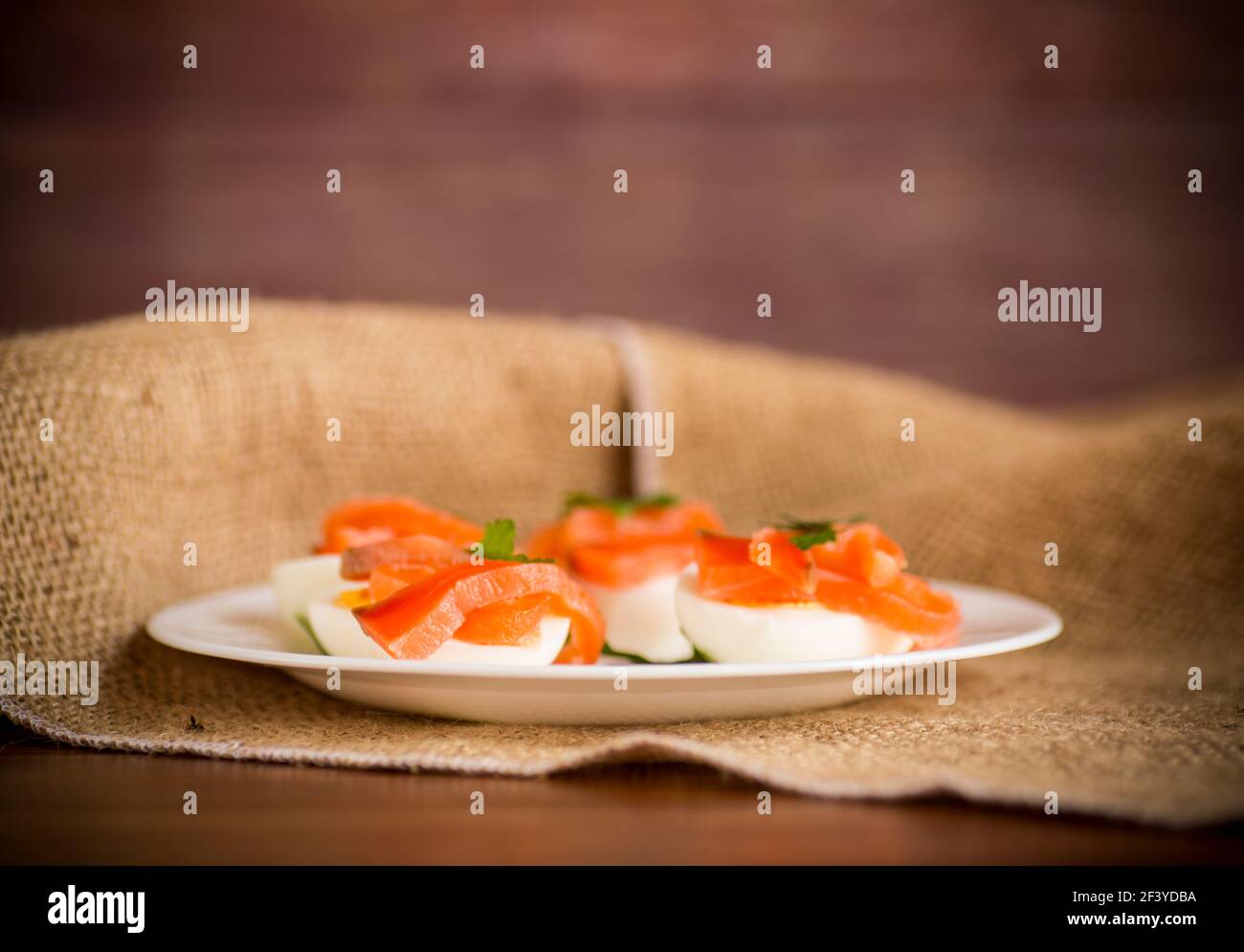 Die Hälfte der gekochten Eier mit den Stücken des gesalzenen Lachses auf Ein Holztisch Stockfoto