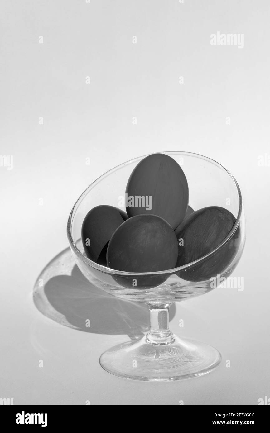 Schwarz-weißer Rahmen. Handbemalte schwarze Ostereier in einer transparenten Glasschale auf hellem Hintergrund, vertikaler Rahmen, Kopierraum, Nahaufnahme, schwarz und w Stockfoto