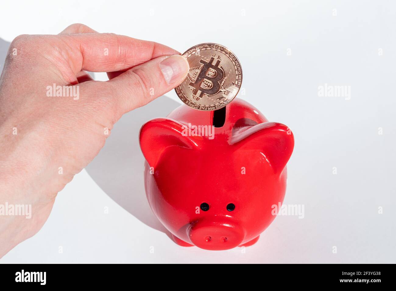 Kryptowährung Sparkonzept. Eine Hand hält eine Bitcoin-Münze über einem roten Sparschwein auf weißem Hintergrund. Neues Finanzsystem. Stockfoto