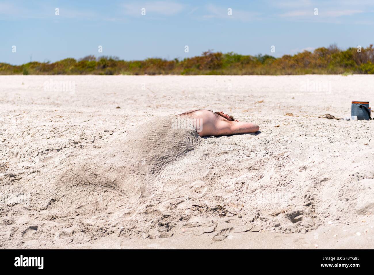 Sanibel Island, USA - 29. April 2018: Bowman's Beach, Florida mit einem lustigen jungen Mann, der als Meerjungfrau mit Muscheln unter Sand begraben ist Stockfoto