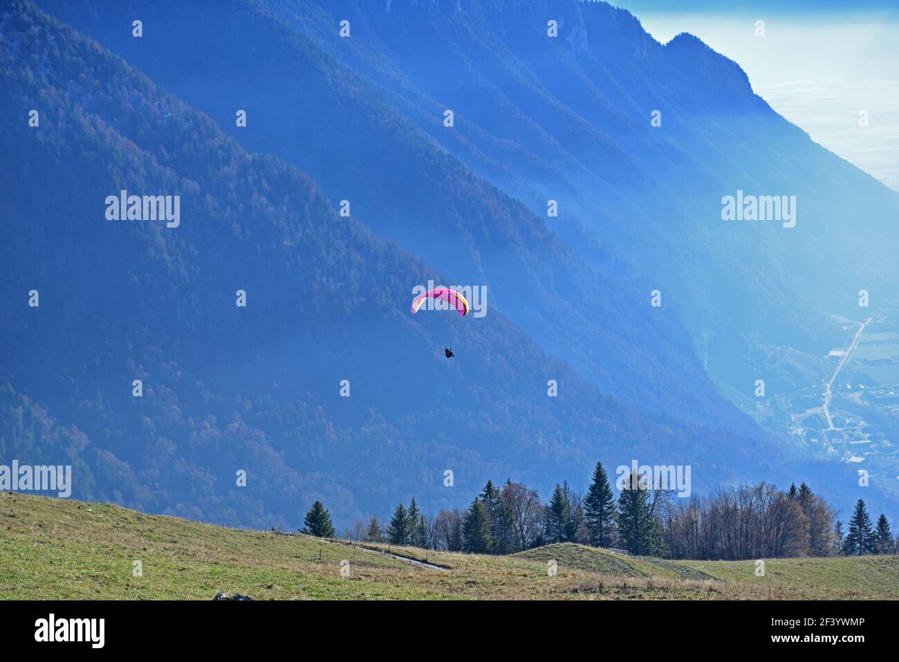 Ein Gleitschirm, der über ein Tal mit einem dramatischen Start Hintergrund der Berge Stockfoto