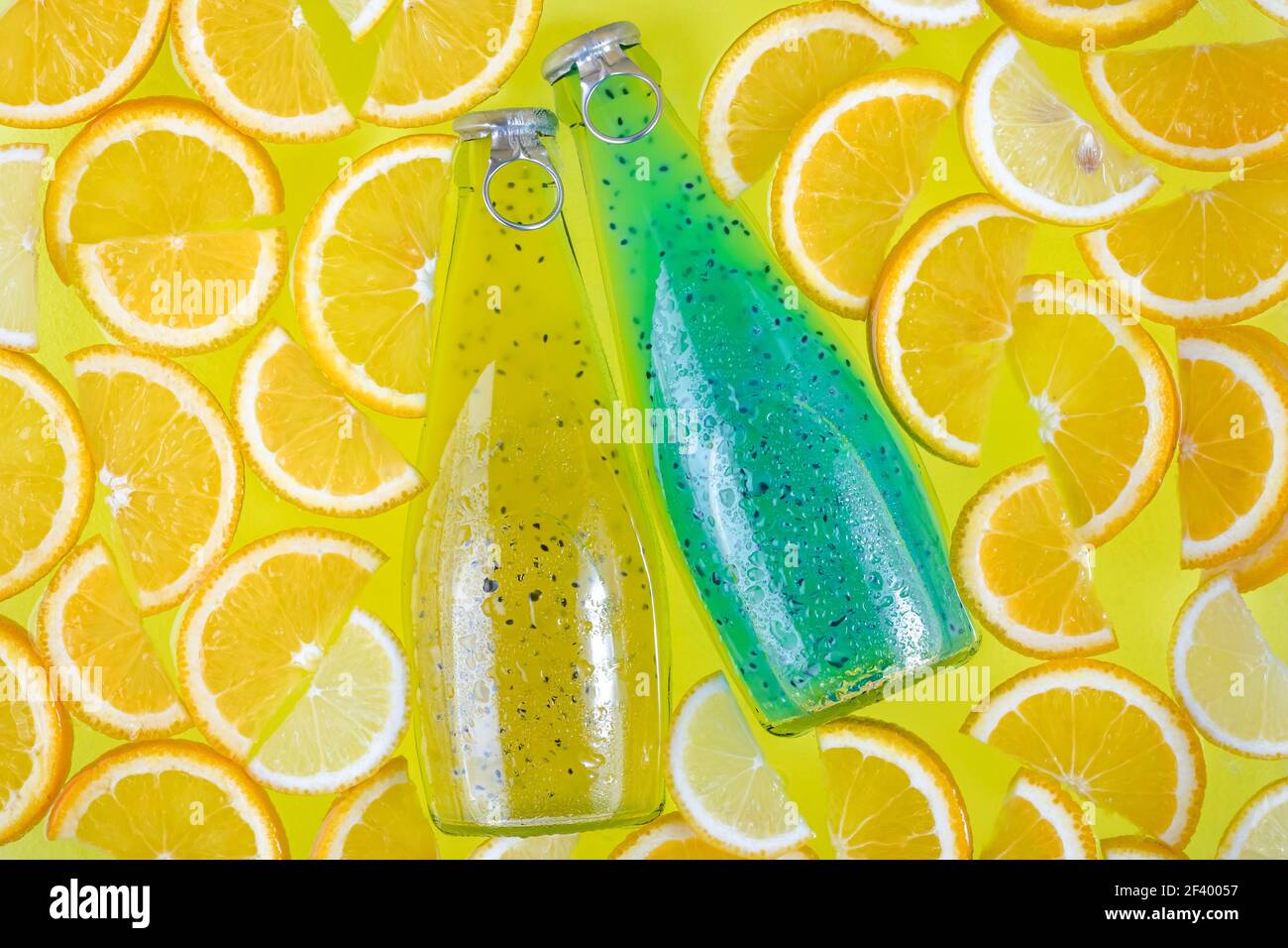 Zwei Glasflaschen auf einem hellen tropischen Zitrushintergrund. Blaue und gelbe Getränke mit Samen. Orangenscheiben, Obst-Smoothie. Getränke in Wasser. Sommer Stockfoto