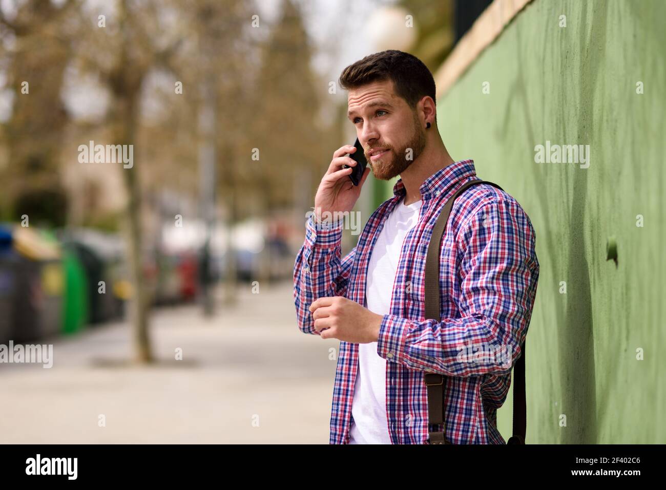 Junger Mann im Gespräch mit seinem Smartphone im städtischen Hintergrund. Leben. Junger Mann im Gespräch mit seinem Smartphone im städtischen Hintergrund. Typ in legerer Kleidung. Lifestyle-Konzept. Stockfoto
