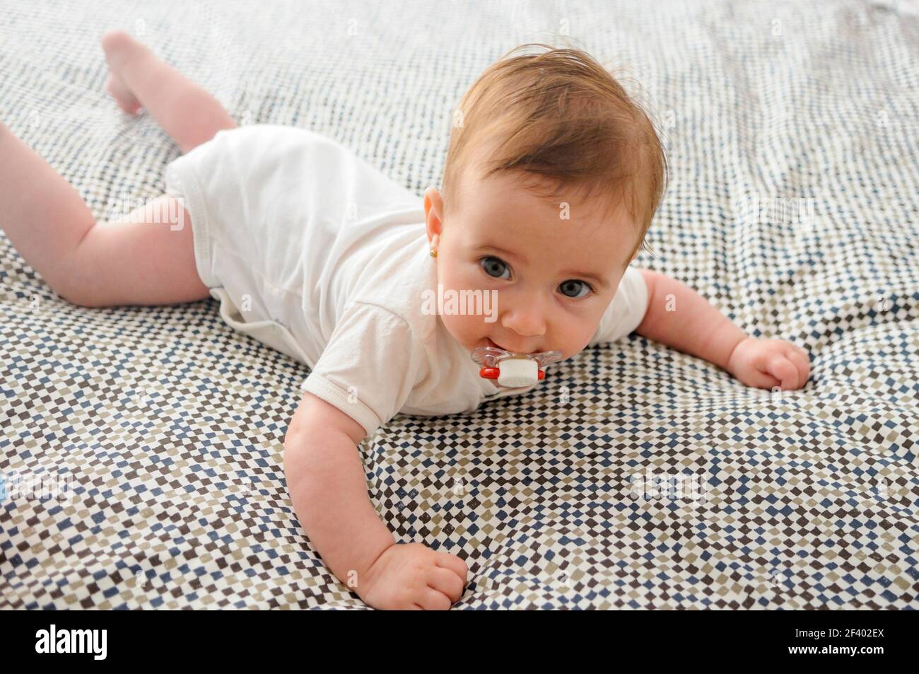 Happy Baby Mädchen, 4 Monate alt, auf dem Bett mit Schnuller. Stockfoto