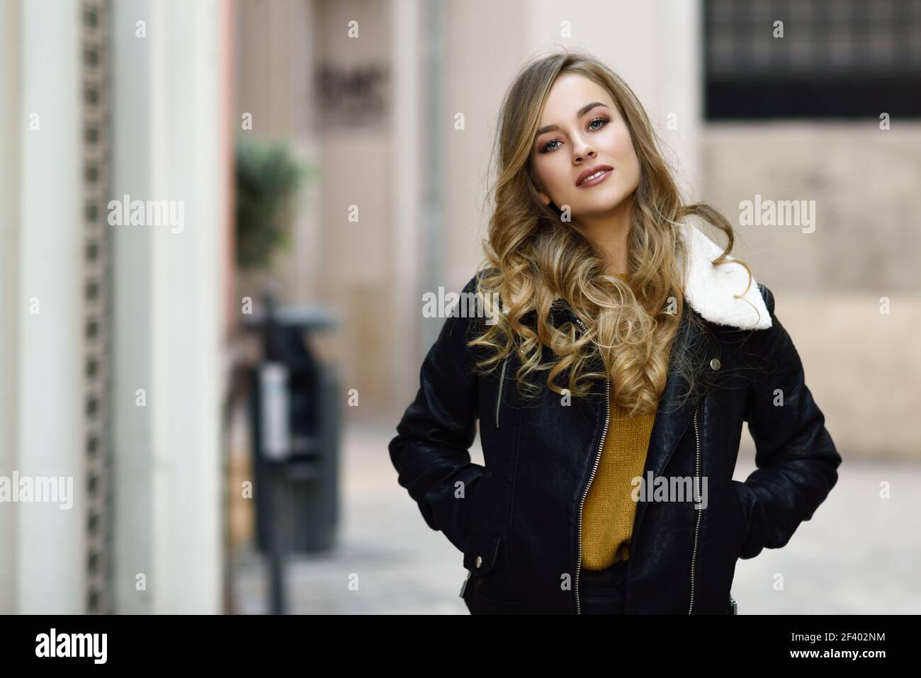 Blonde Frau im städtischen Hintergrund. Schöne junge Mädchen mit schwarzen leder jacke und mini rock auf der Straße stand. Hübsche Russische Frauen mit langen gewelltes Haar frisur und blaue Augen. Stockfoto