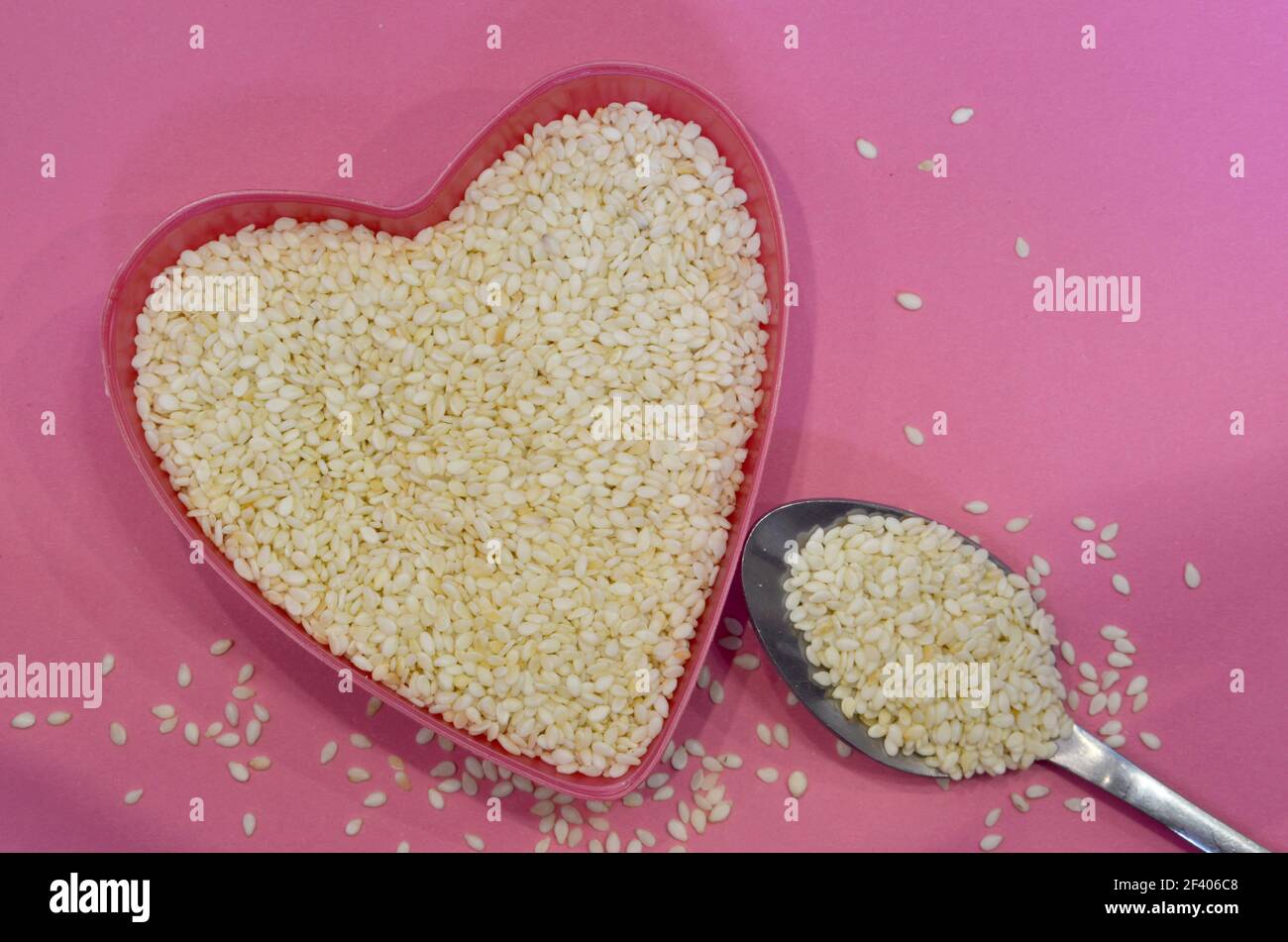 Weiße Sesamsamen in Herzform auf rosa Hintergrund, Draufsicht. Super Essen Zutat. Gesundes veganes Konzept Stockfoto