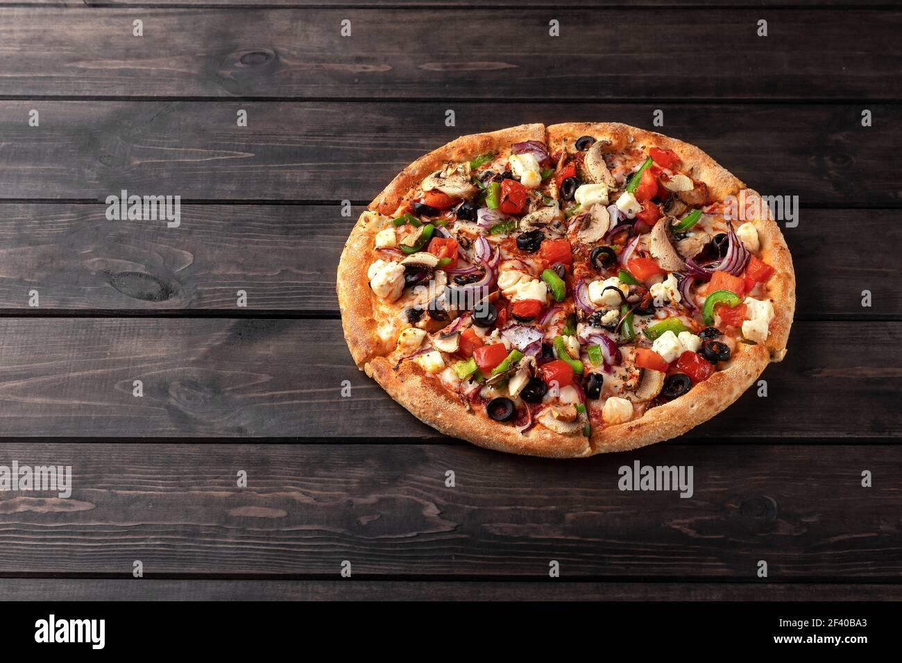 Ganze frische runde Pizza mit Hühnerfleisch, Gemüse, Pilze und Käse close-up auf einem hölzernen braunen Tisch. Leckere Fast-Food-Hintergrund in Pizzeria w Stockfoto