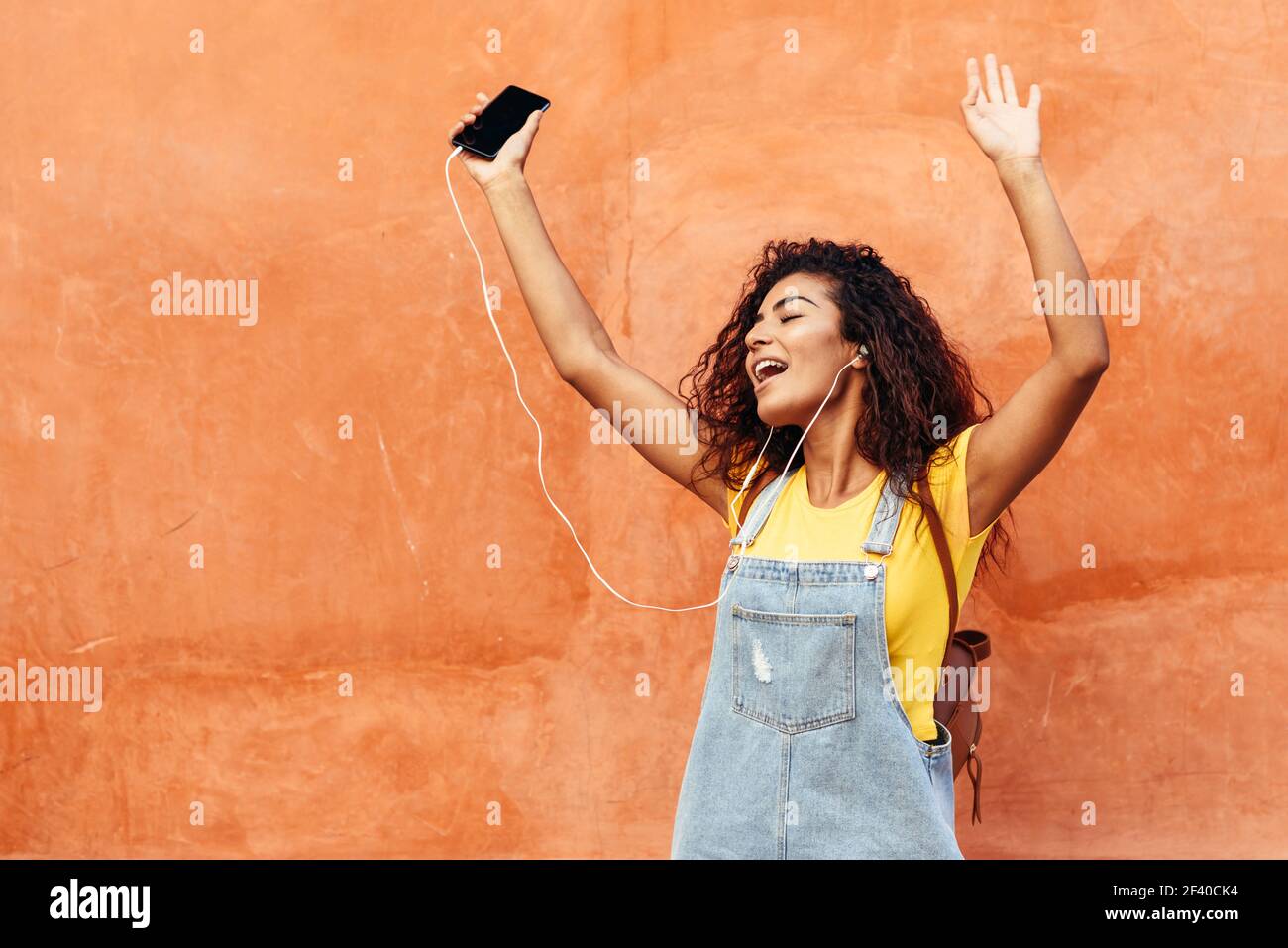 Gerne Arabische Mädchen Musik hören und tanzen mit Ohrhörer im Freien. Afrikanische Frau in Freizeitkleidung mit Curly Frisur im städtischen Hintergrund. Stockfoto