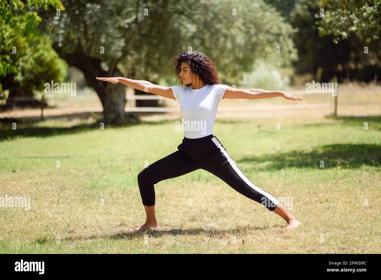 Junge arabische Frau Yoga in der Natur. Afrikanische Frauen tragen sportliche Kleidung tun Krieger II Abbildung im städtischen Park. Stockfoto