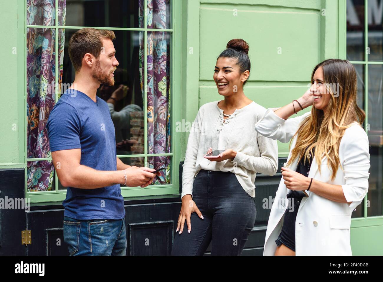 Drei multiethnischen Menschen lachen im Freien mit smart phone in ihren Händen. Multiethnische Gruppe von Freunden Spaß im städtischen Hintergrund. Stockfoto