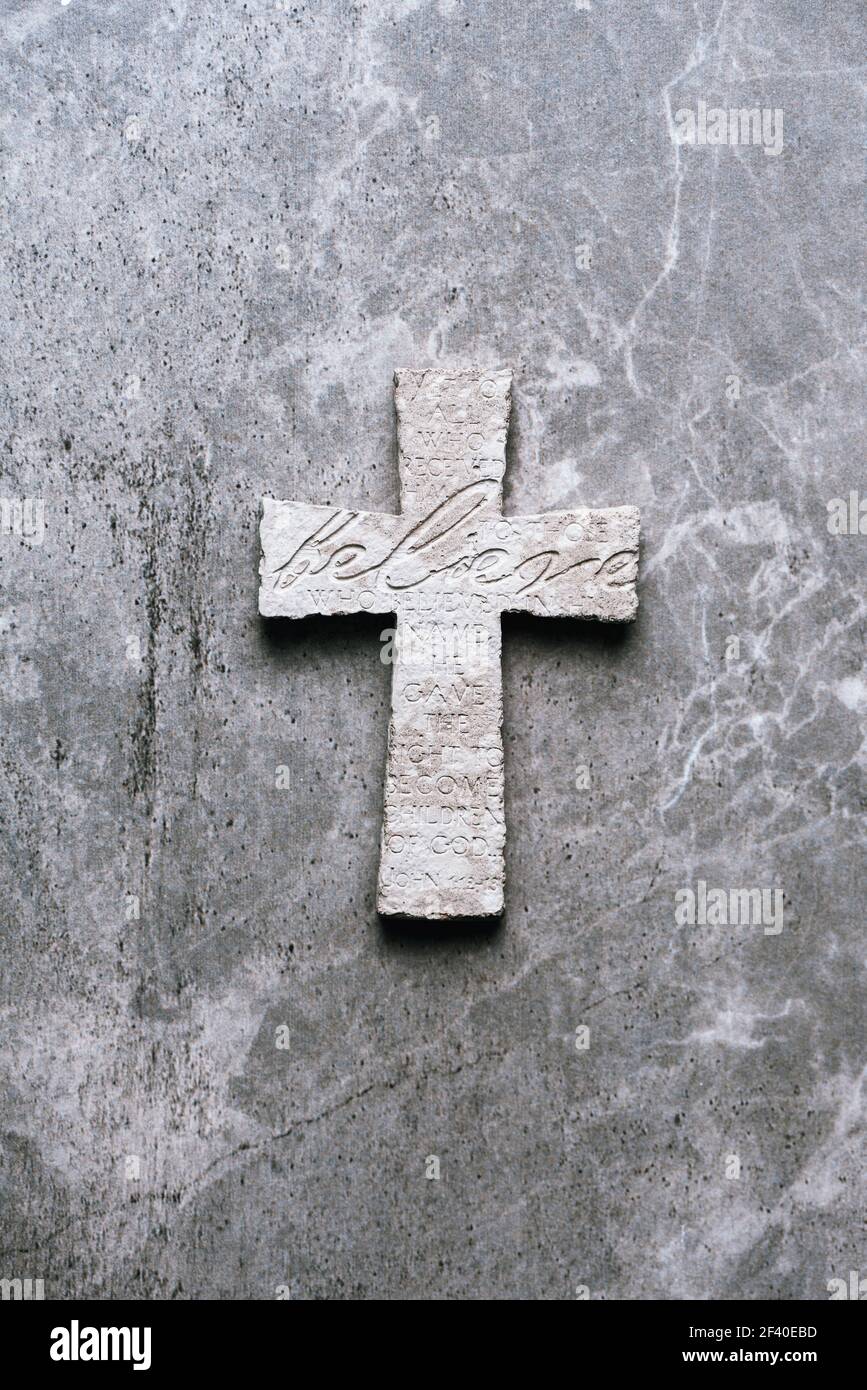 Steinkreuz mit Inschrift glauben auf grauem Hintergrund, Copy Space. Christlicher Hintergrund. Biblischer Glaube, Evangelium, Heilskonzept Stockfoto