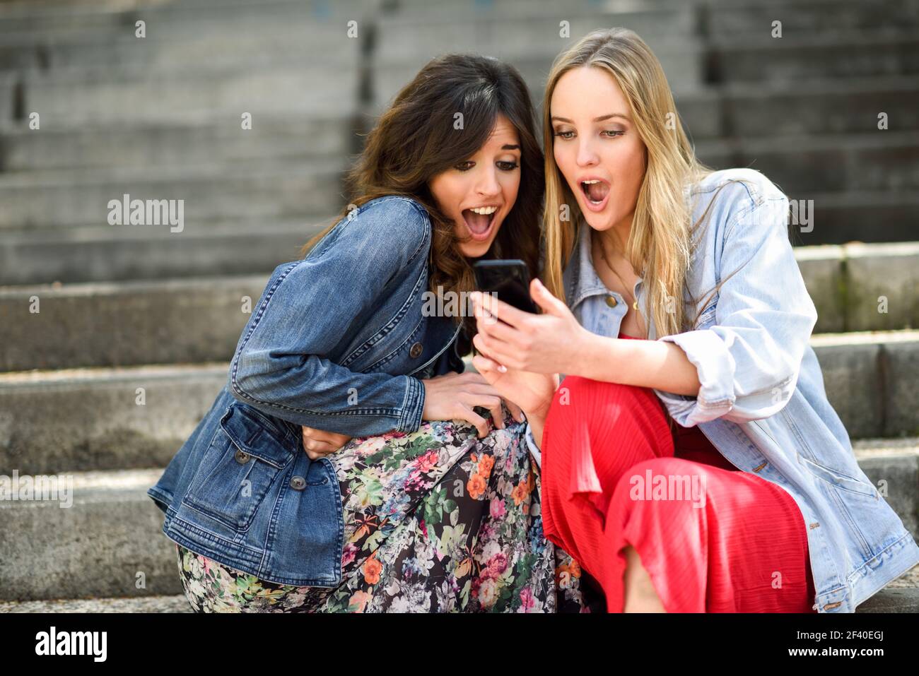 Zwei junge Frauen durch, was Sie auf Ihrem smart phone draußen sehen, staunen, sitzen auf den städtischen Schritte. Freunde Mädchen. Stockfoto